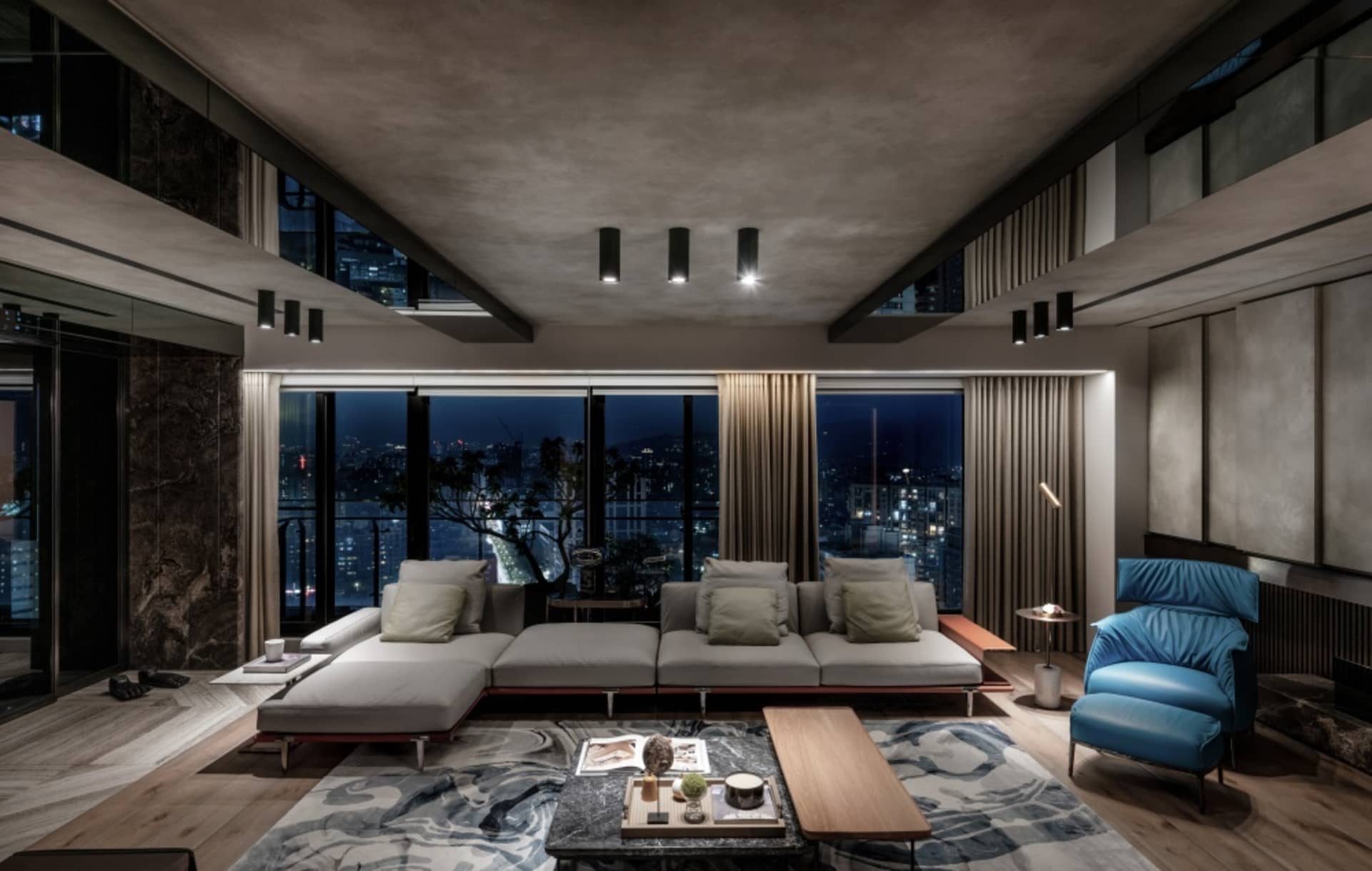 Modern living room featuring a large sofa and floor-to-ceiling windows overlooking a cityscape at night.