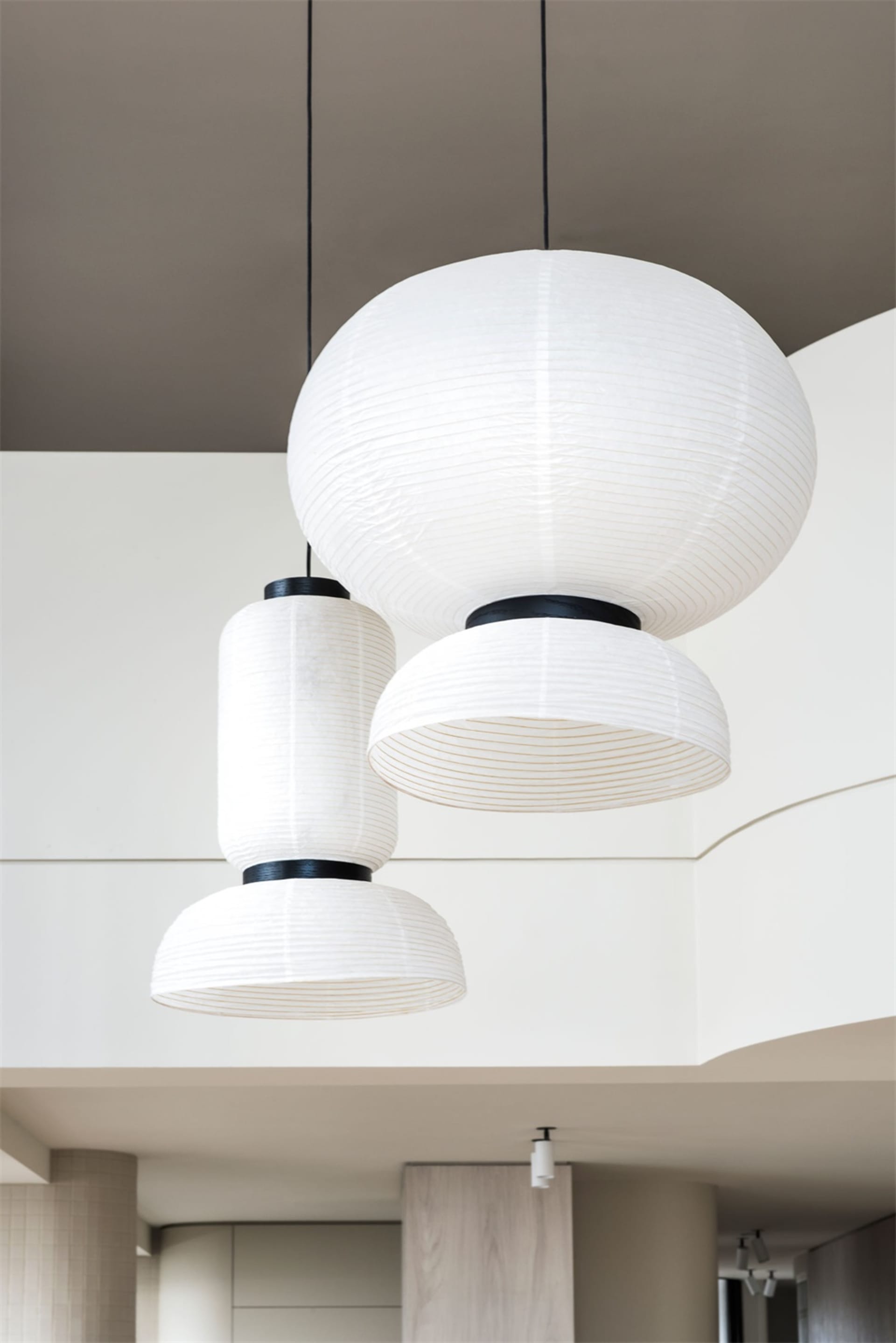 Three modern hanging lamps made of paper, with black accents, suspended from a neutral ceiling in a minimalist interior desig