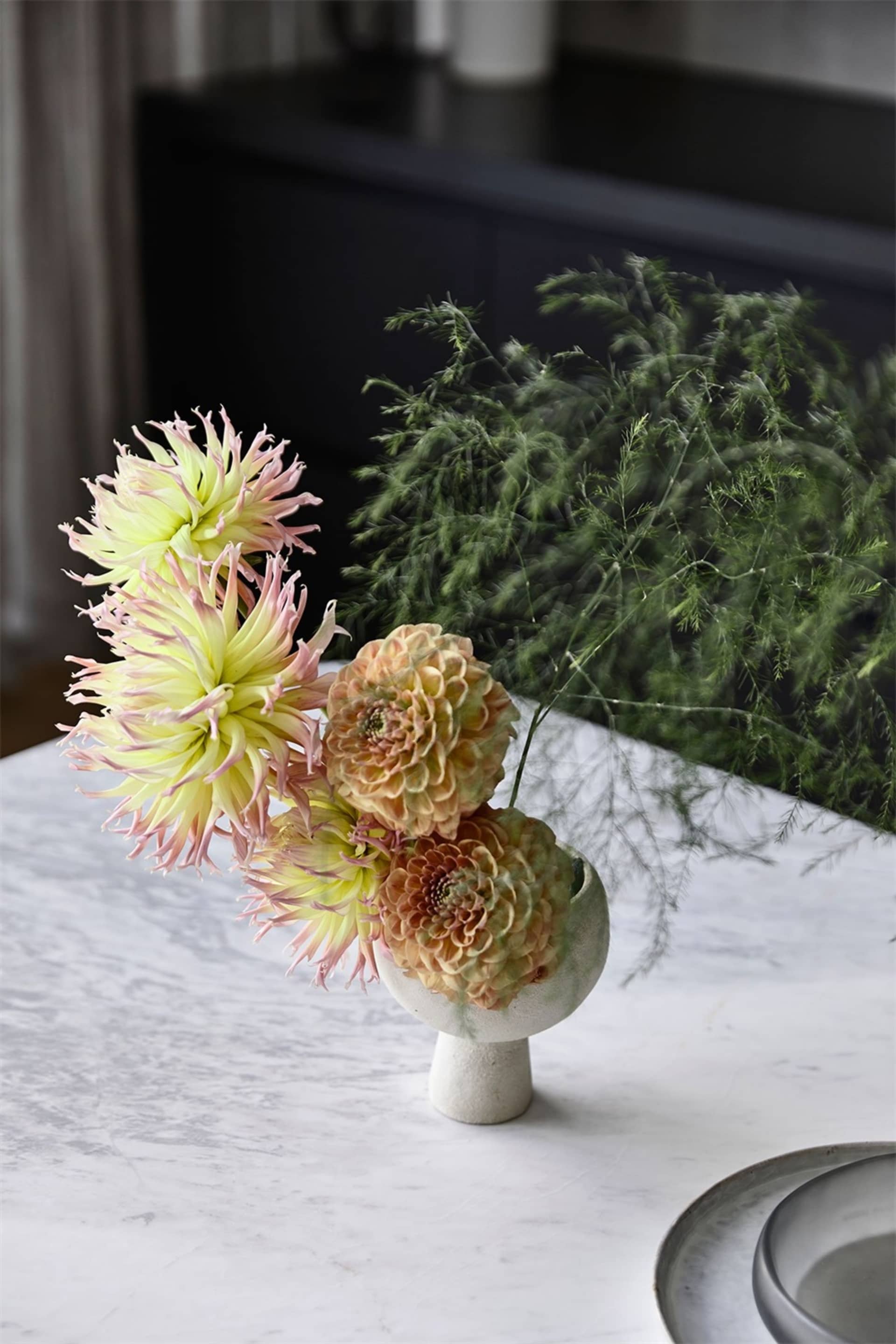a bouquet of delicate flowers arranged in a modern vase, placed on a marble surface.