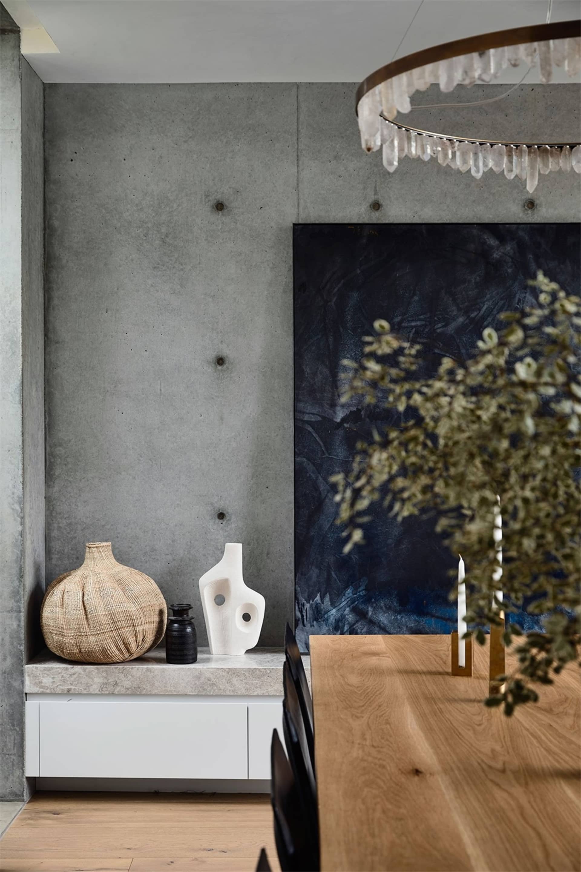 Modern minimalist interior featuring a concrete wall with abstract sculptures and a chandelier.