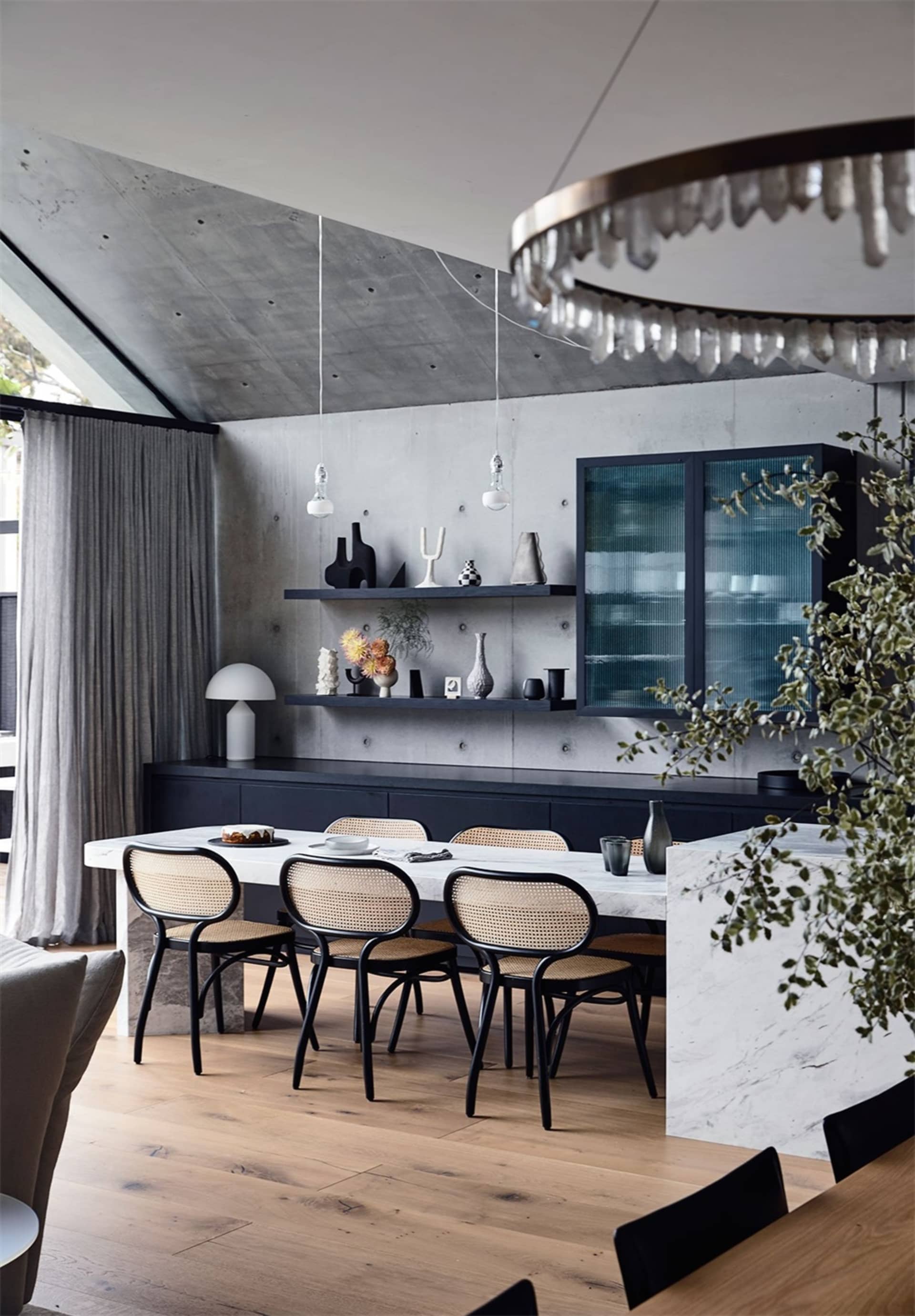 A modern dining room featuring a table, chairs, and decorative shelving against a concrete wall.