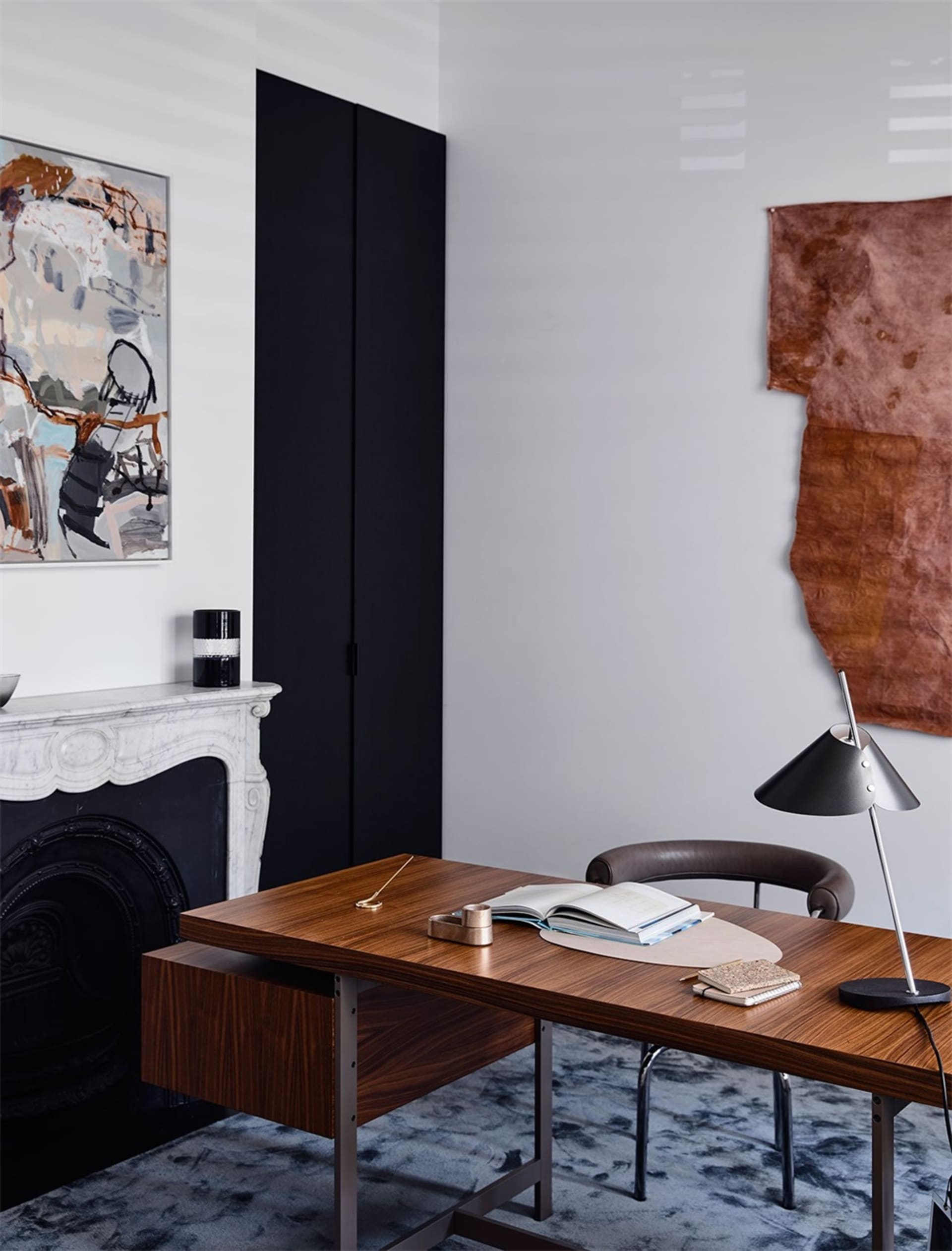 A modern study room featuring a wooden desk, leather chair, and abstract and textured wall hangings.