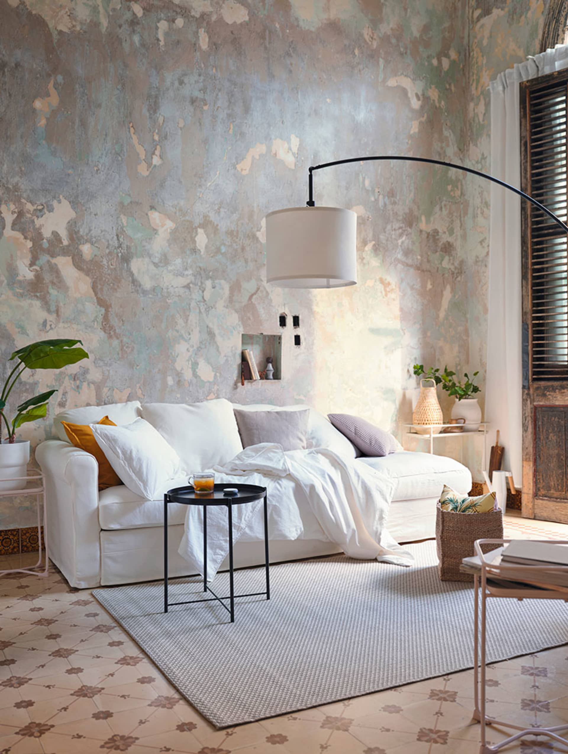 A minimalist living room with a white couch, white rug, and a lamp on a black side table.