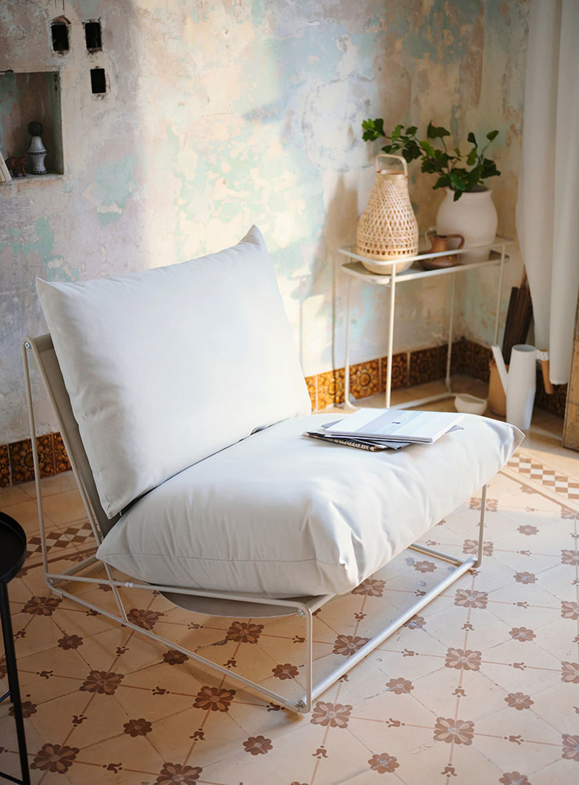A minimalist living room with fabric cushions on a white metal chair.