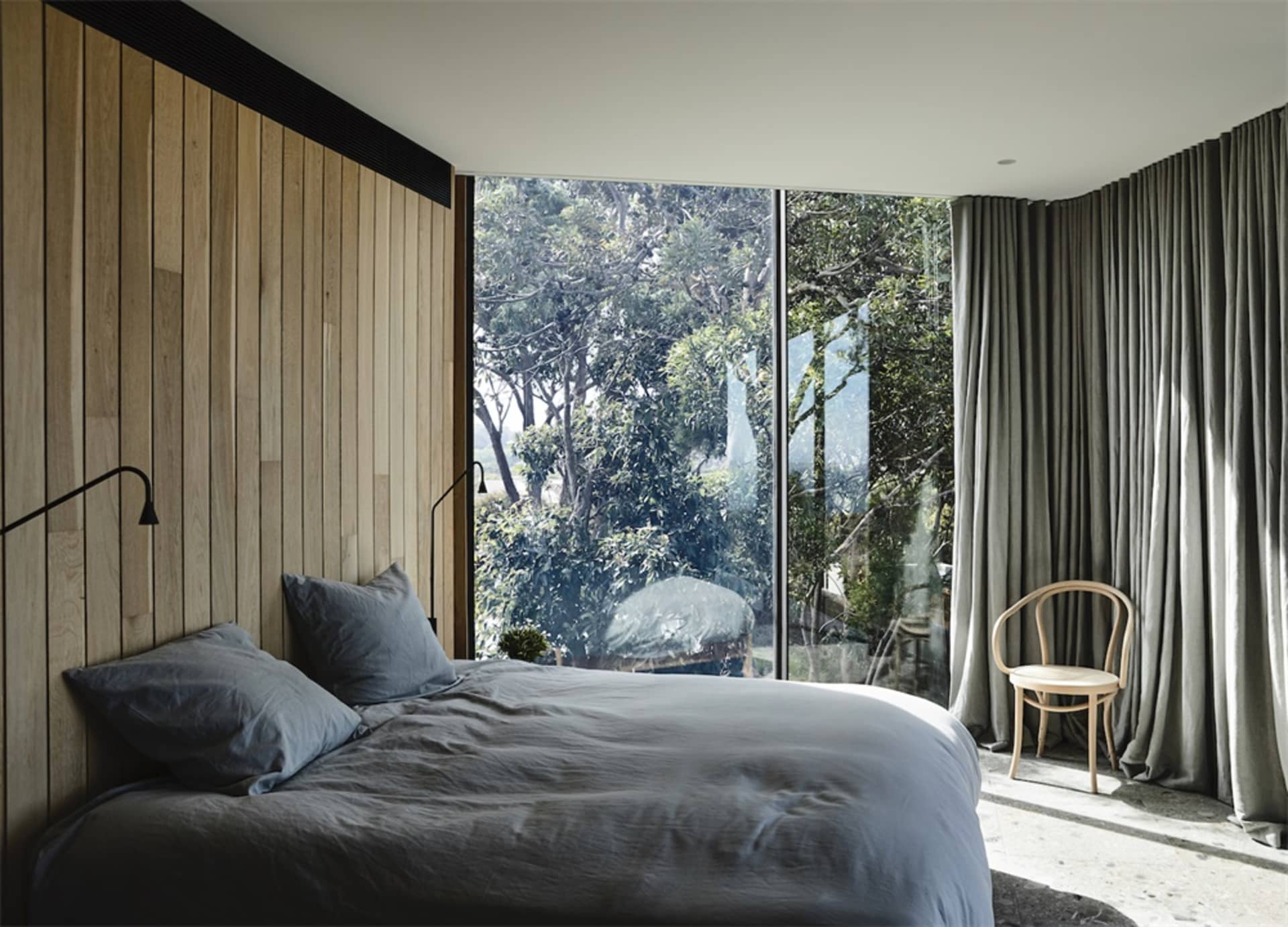 Minimalist bedroom featuring a bed with wood paneling, glass windows, and a gray fabric headboard.