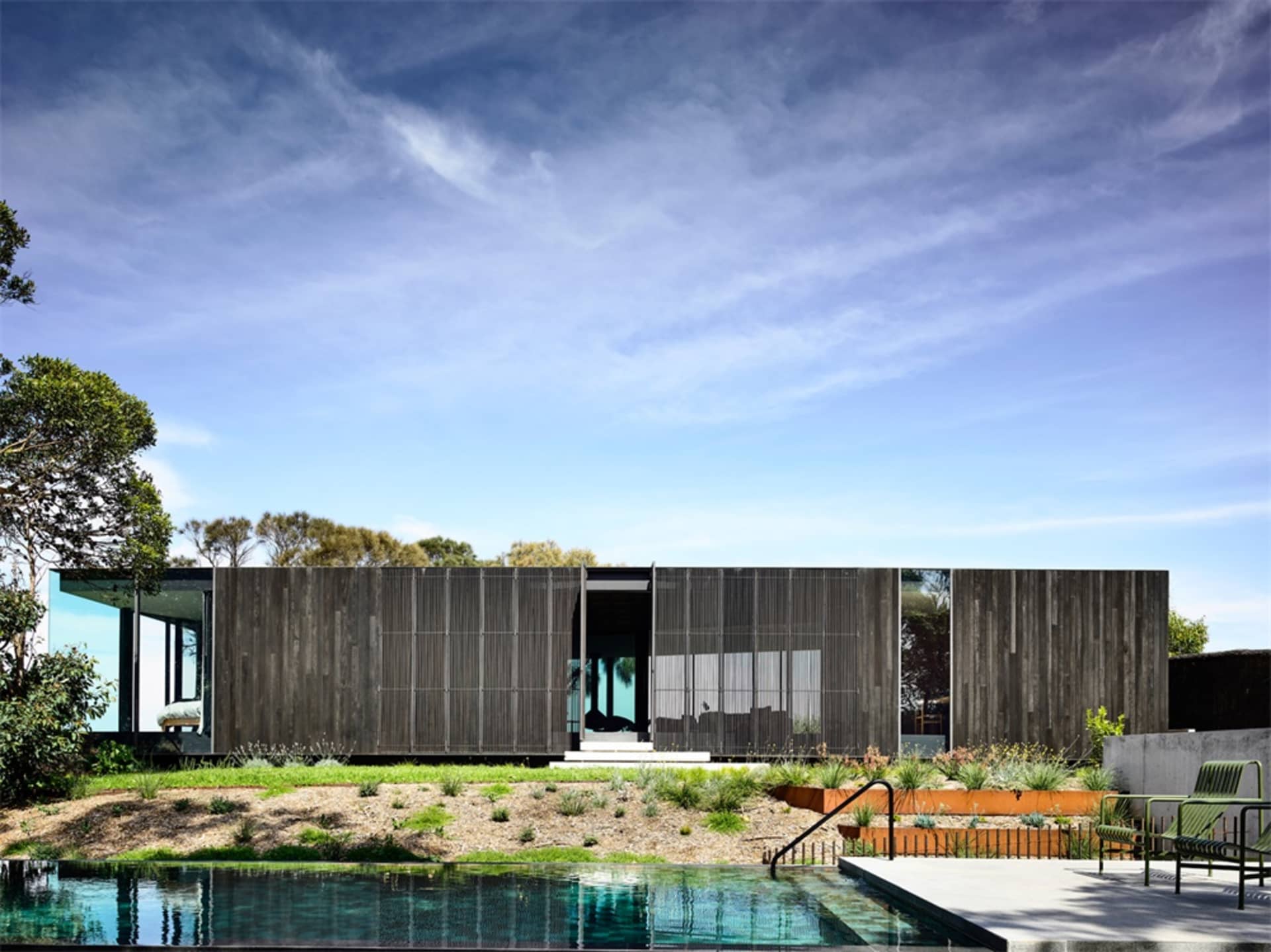 A modern house with wooden exterior walls and a large pool in the foreground.