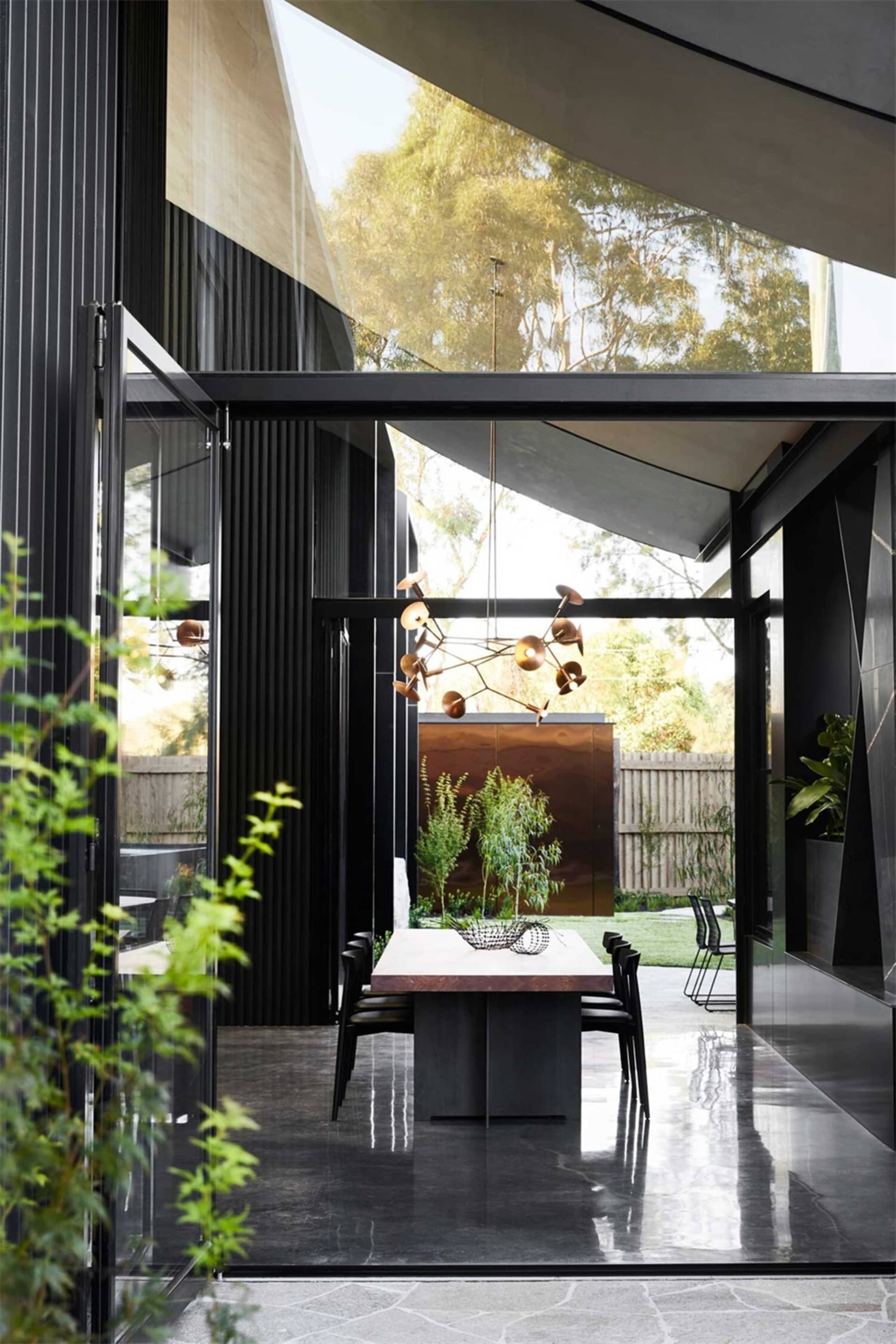 A modern dining room featuring concrete folding doors, a wooden dining table, and a unique pendant light hanging from the cei