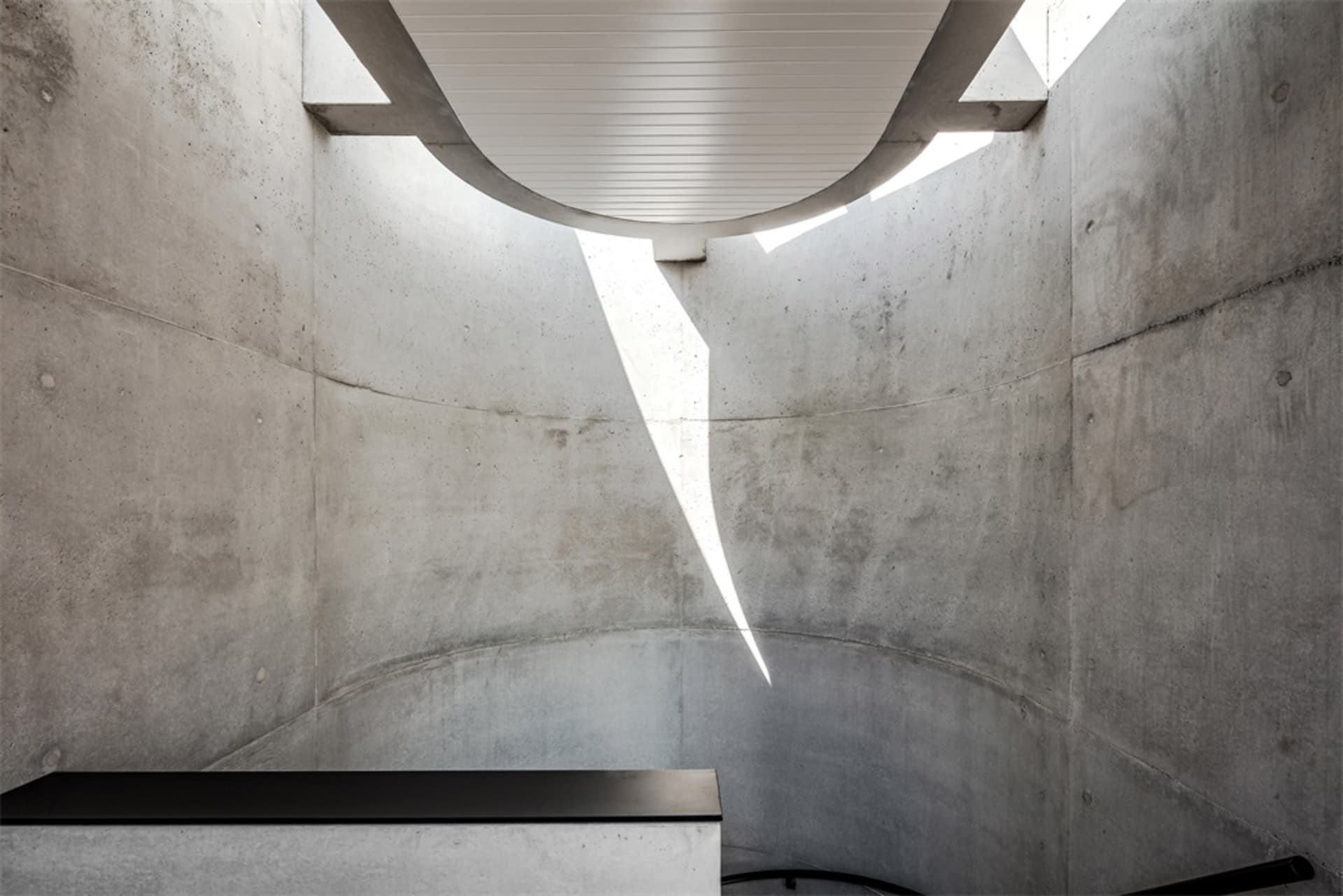 A minimalist concrete interior space with a white ceiling and a black platform.