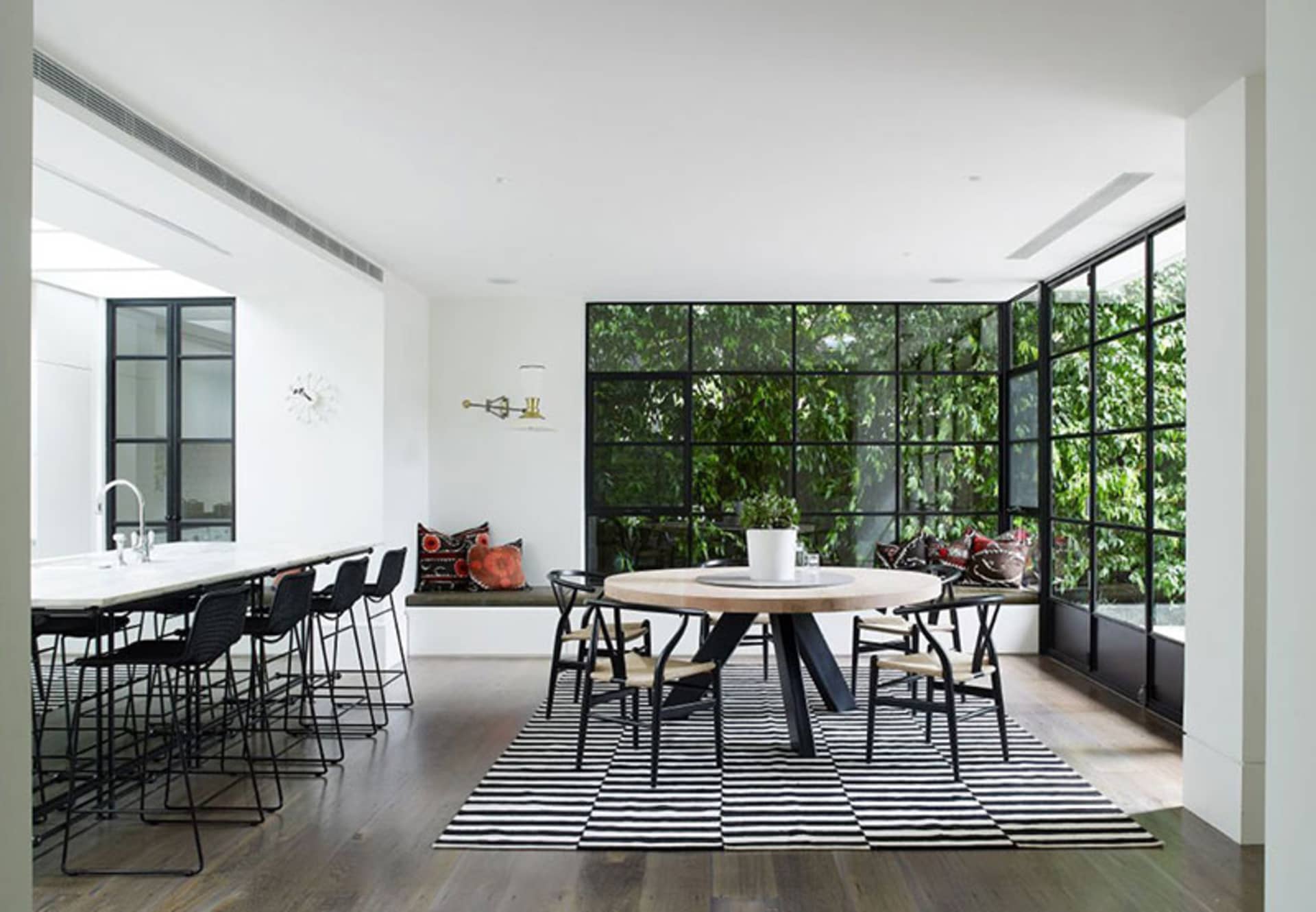 A modern kitchen dining room featuring black metal chairs around a round dining table with marble top, set on a black and whi