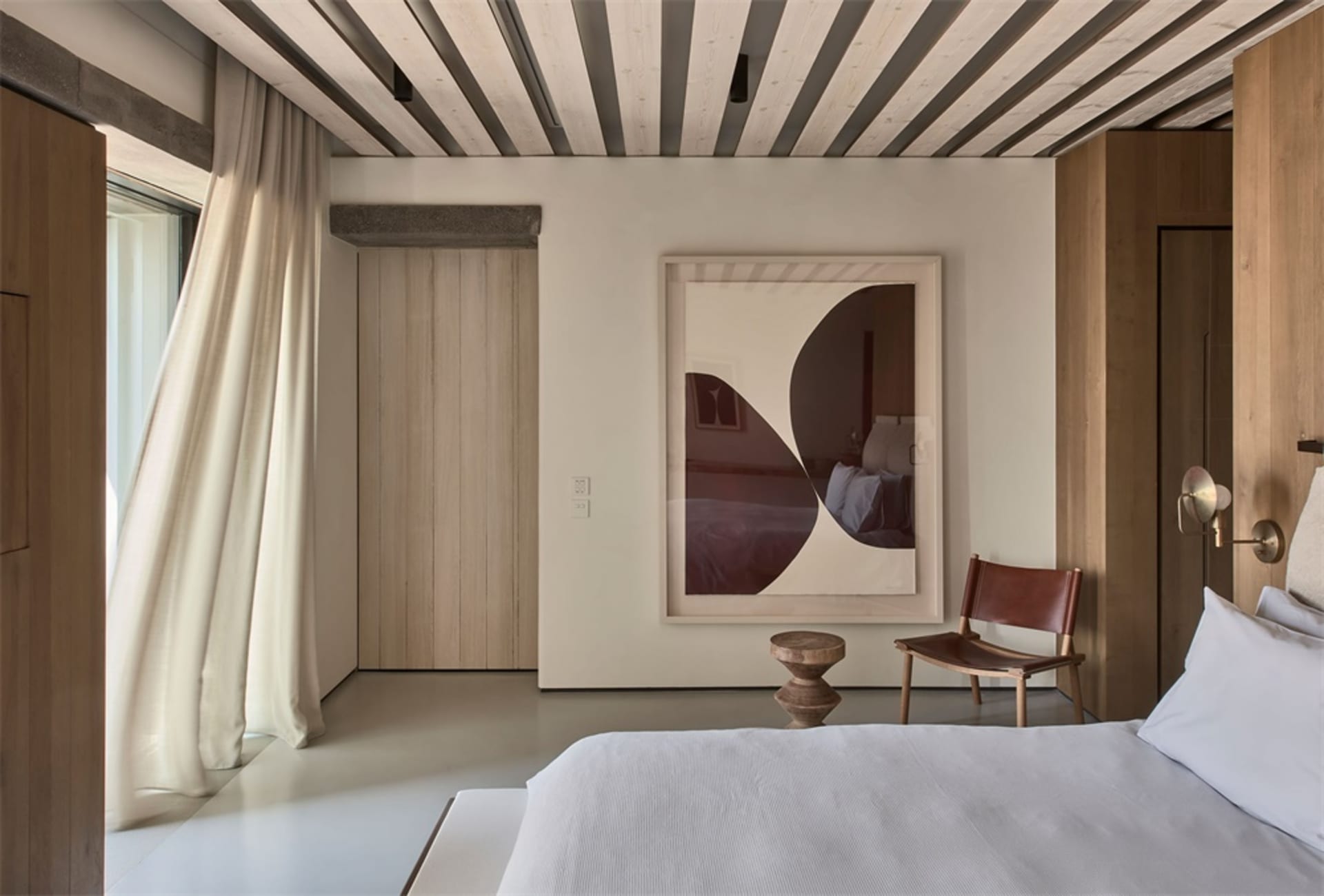 A minimalist bedroom with wood furnishings, leather accents, and a large window with curtains.