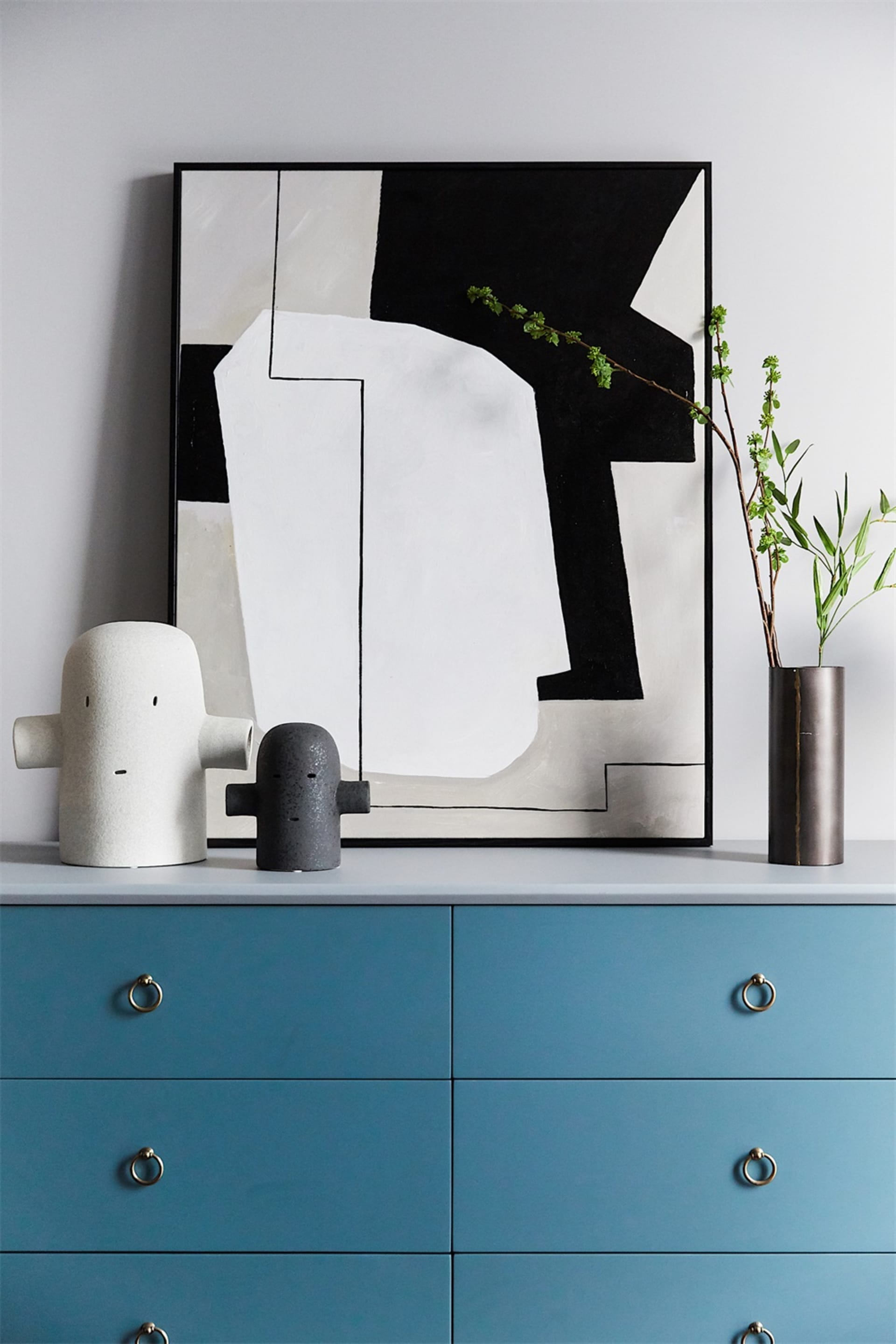 A blue dresser with ceramic storage objects and a black and white abstract painting.
