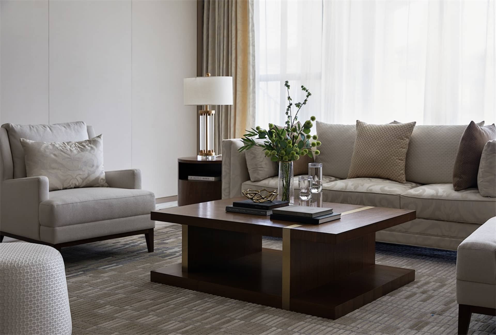 A modern living room featuring a wooden coffee table with books and flowers, a beige armchair, and a white sofa with throw pi