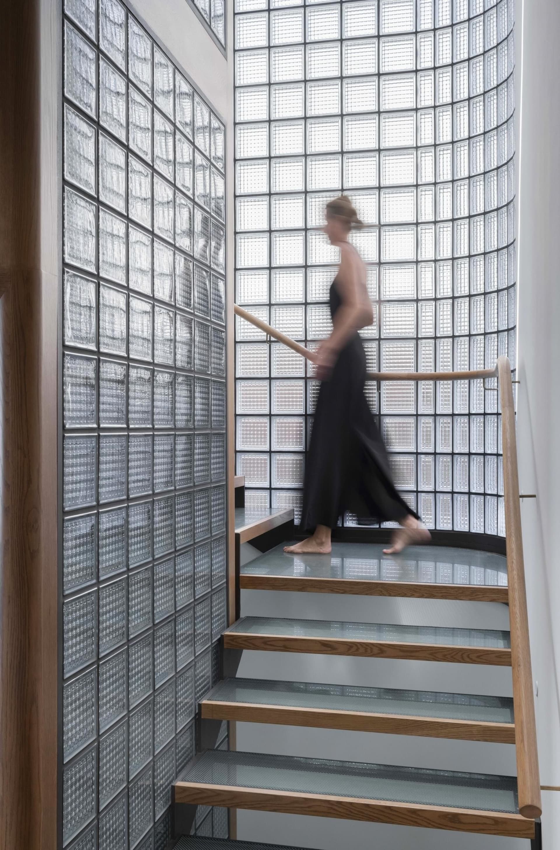A modern interior with wooden and glass stairs leading up to a curved glass wall.