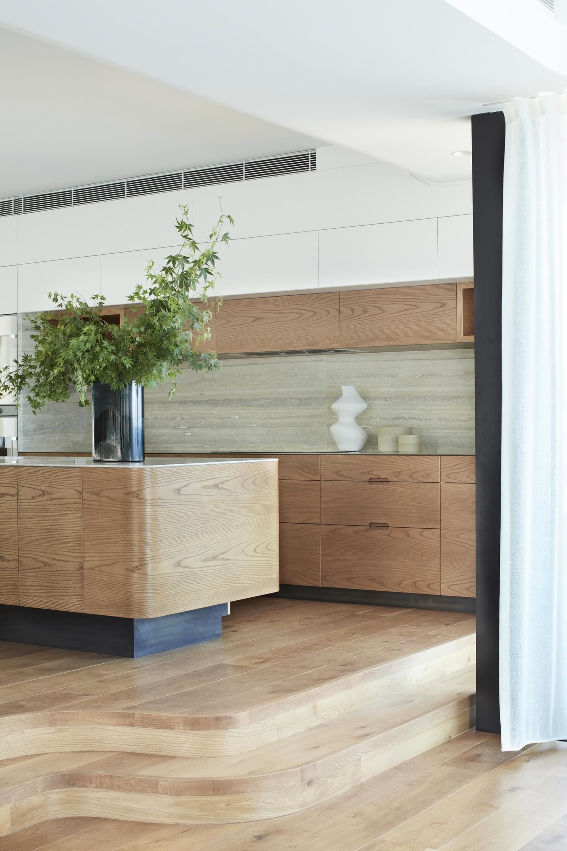 A modern kitchen interior featuring wooden cabinets and a natural wooden floor.
