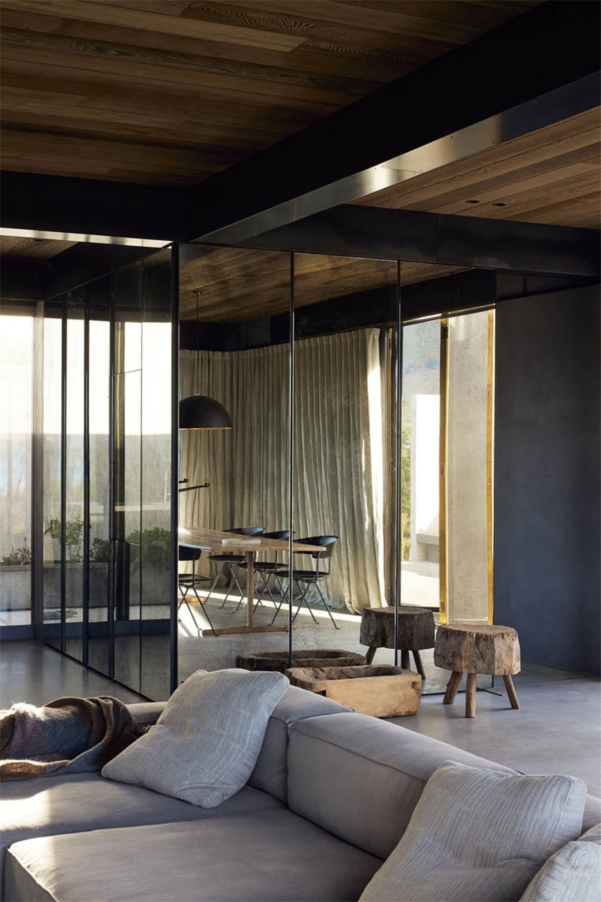 Industrial-style living room with grey sofa, wooden stools, and glass windows.