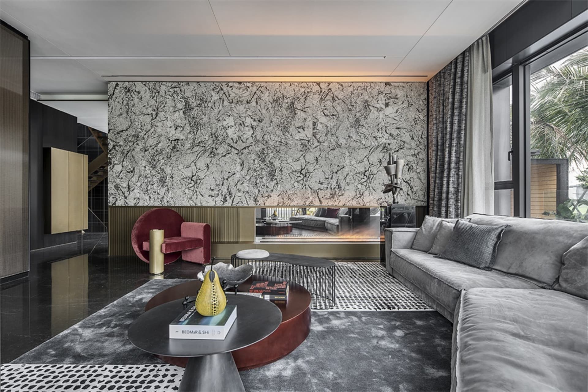 A modern living room with a marble wall and a gray sofa with a patterned rug and round tables.