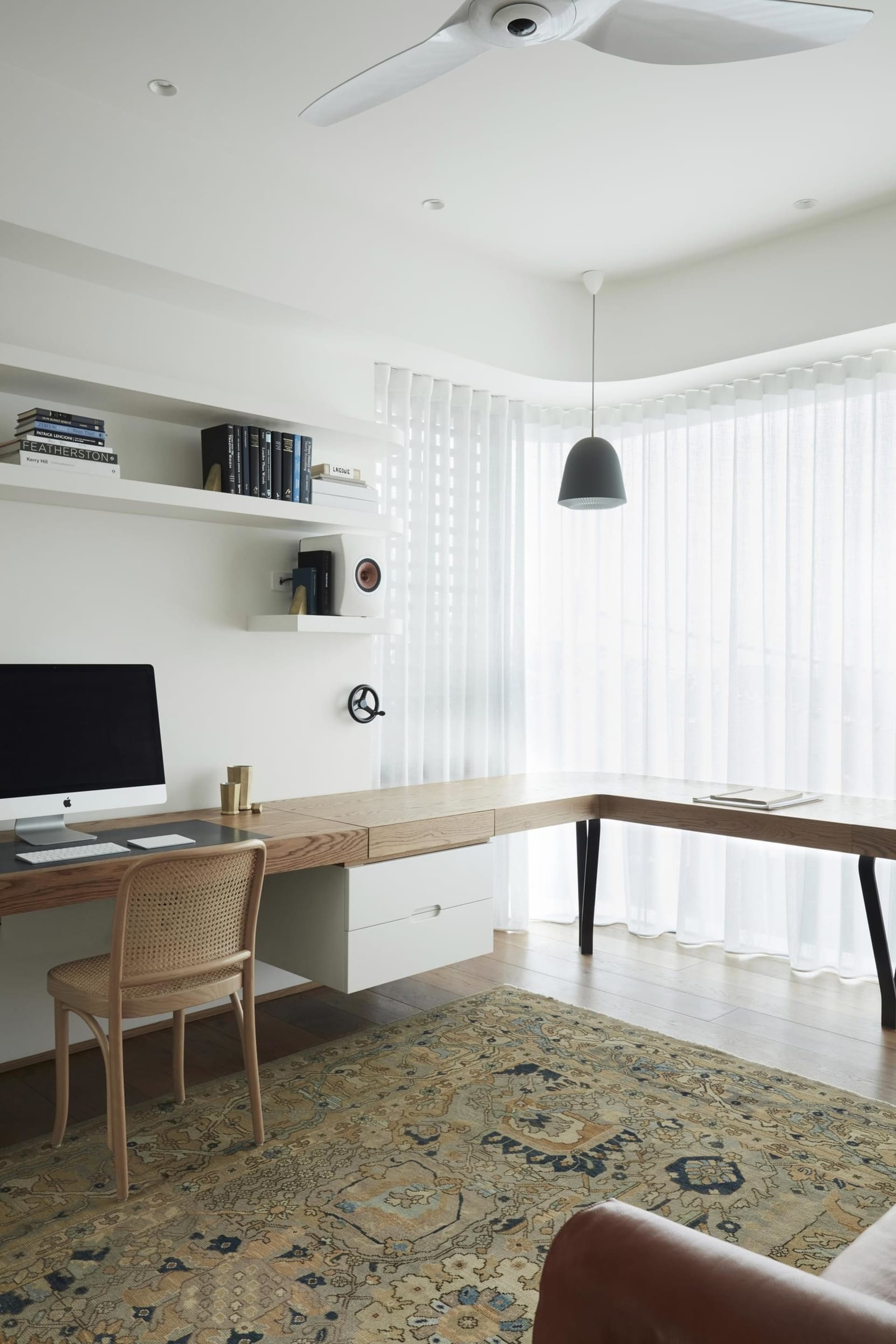 A minimalist home office featuring a wooden desk, leather armchair, and patterned rug.