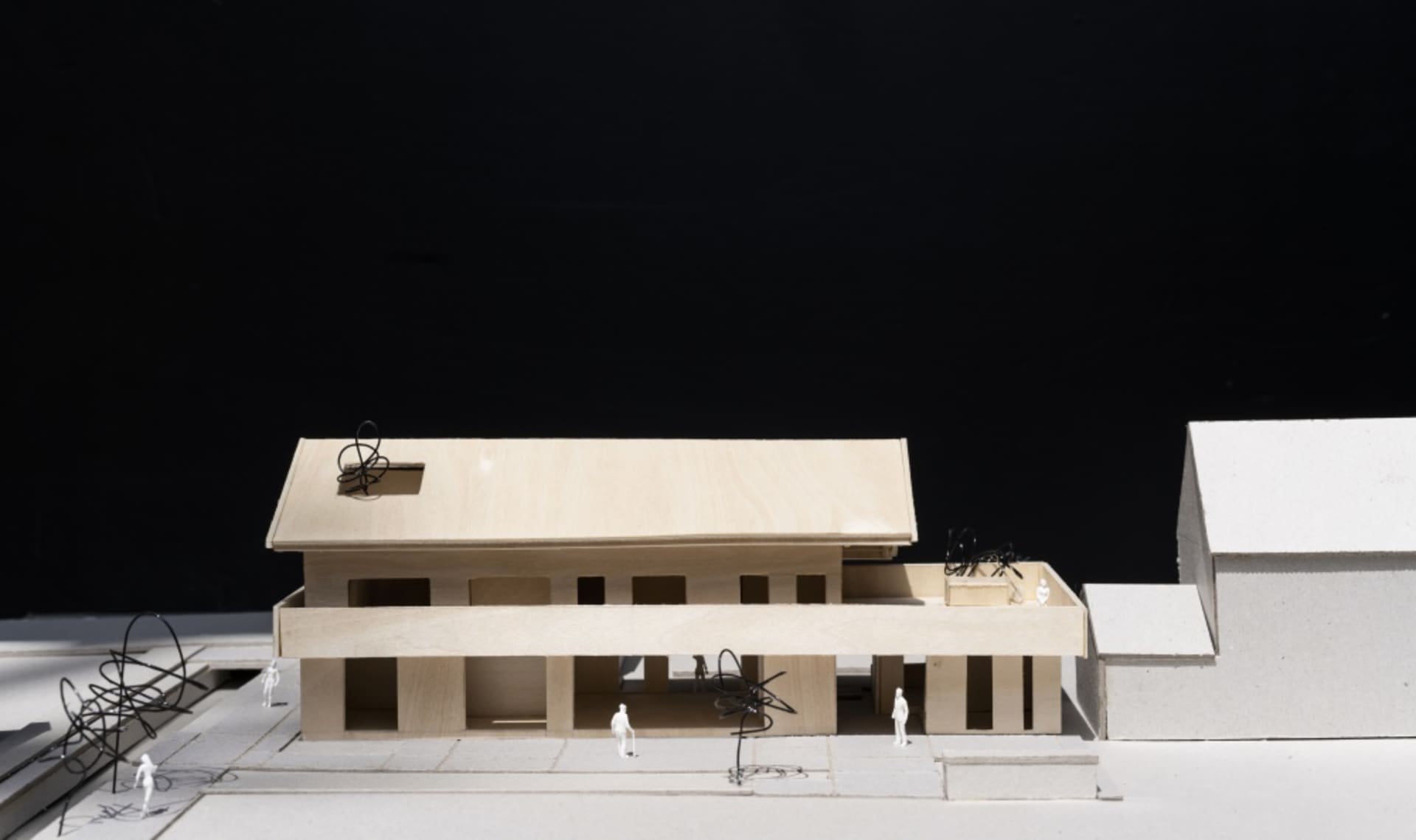A wooden architectural model of a modern building with an open floor plan and outdoor seating.