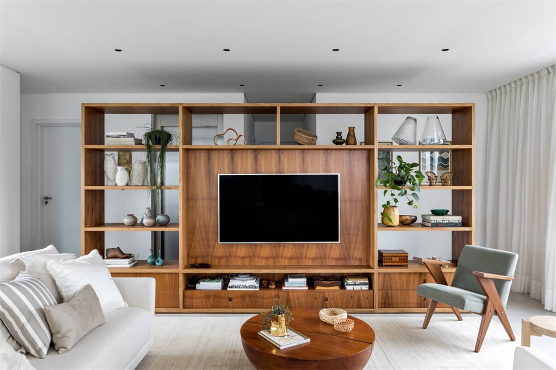 A modern living room with a wooden entertainment center, white furniture, and minimalist decor.
