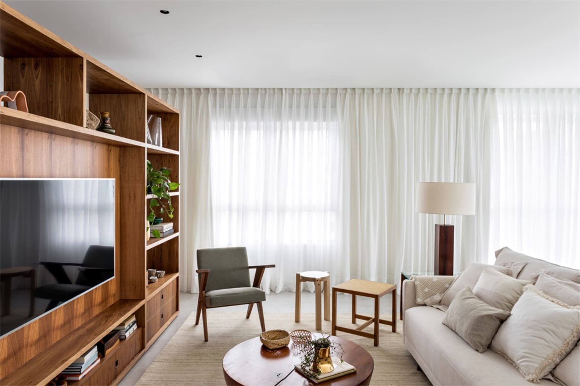 A modern living room featuring wooden shelving, a comfortable sofa, and a large window with white curtains.