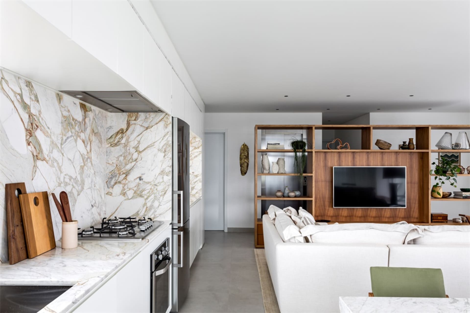 A modern open-concept living and kitchen area with marble countertops, wooden furnishings, and stainless steel appliances.