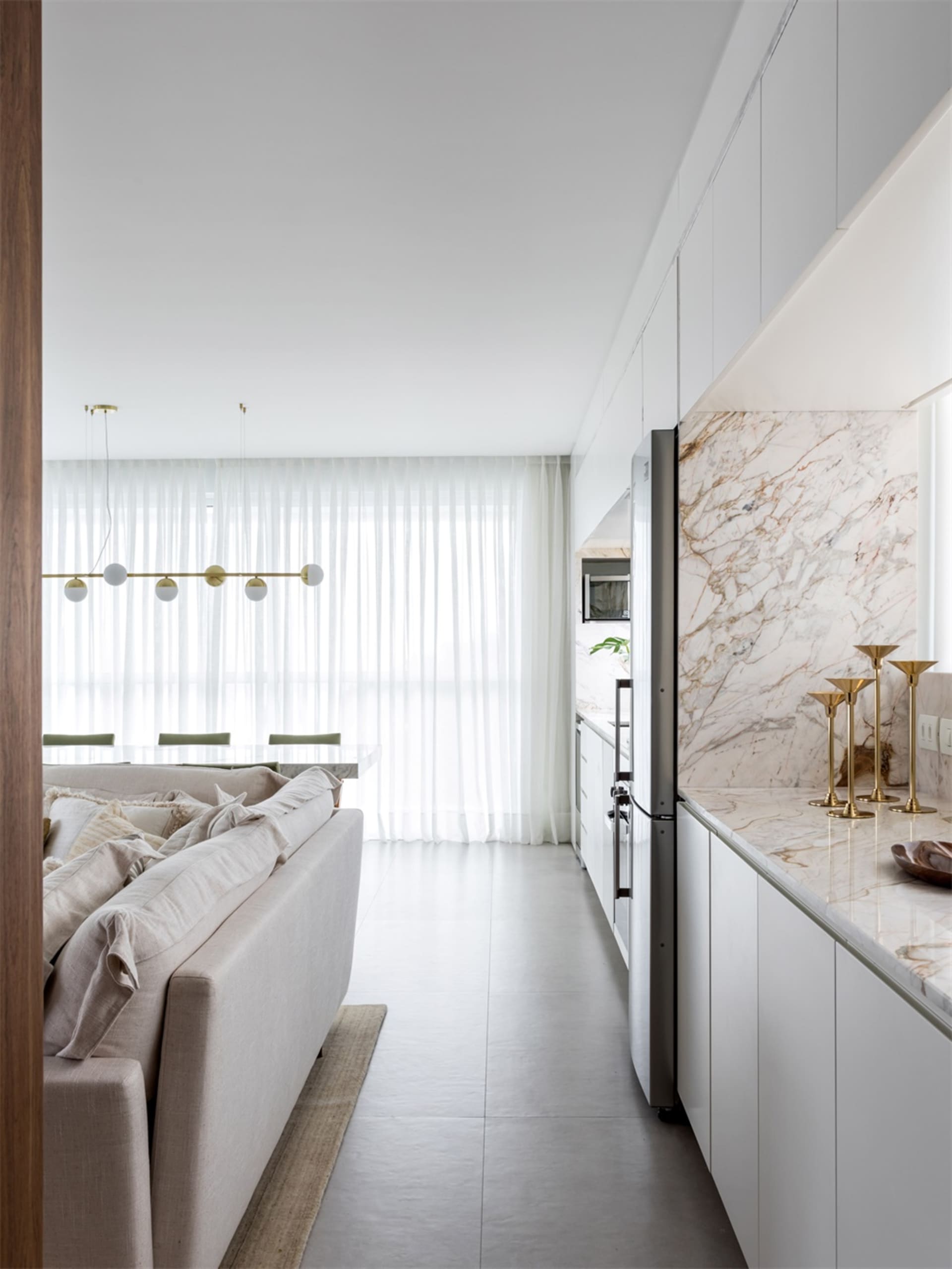 Modern minimalist open-plan living and dining area with white marble countertops, backsplash, and floor, steel kitchen applia