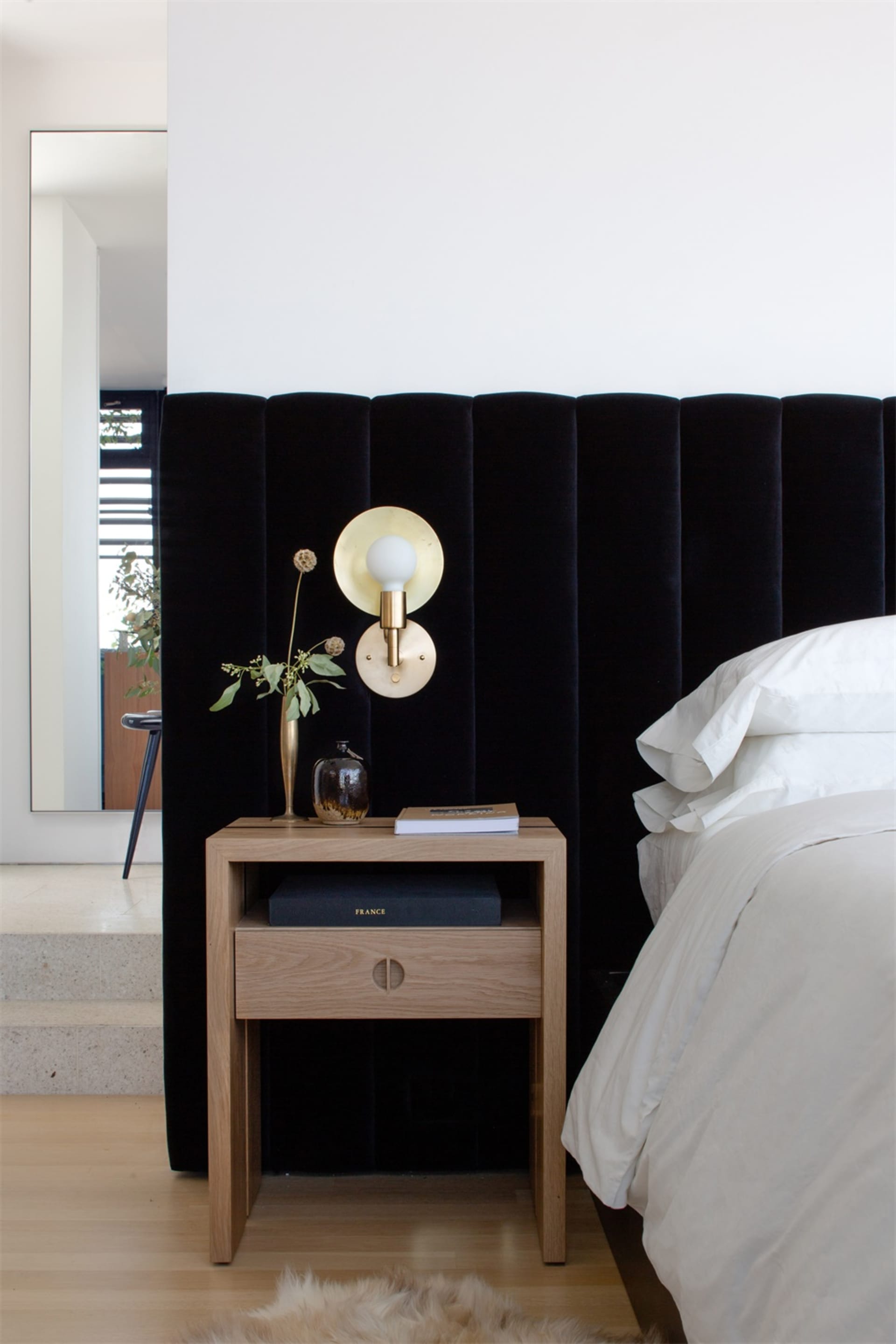 A modern bedroom featuring a black upholstered headboard, wooden nightstand, and brass lamp.