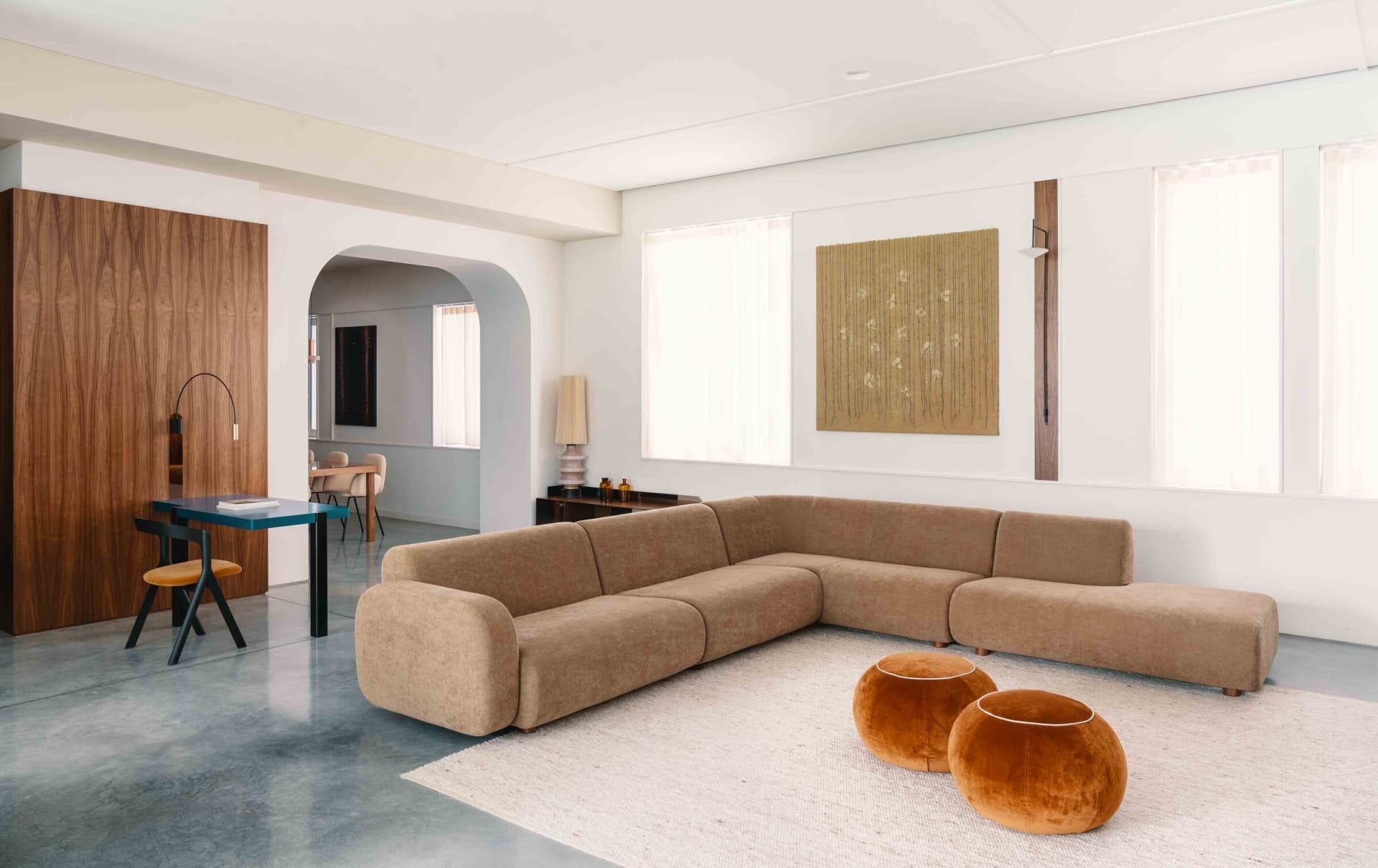 Modern living room with a beige fabric sectional sofa, two orange poufs, and a tall lamp on a low table, set against a white