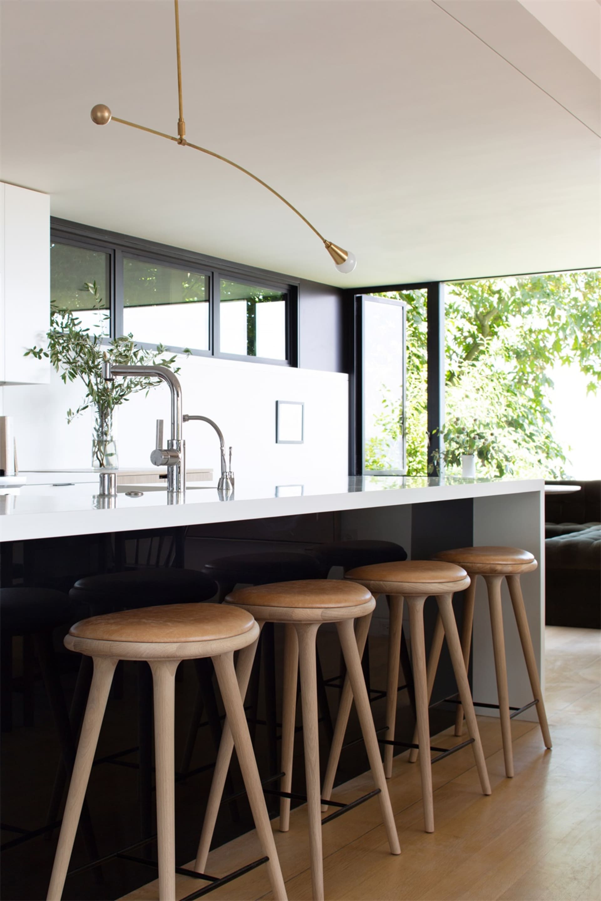 A modern kitchen featuring wooden stools and a white countertop with a sink and faucet.