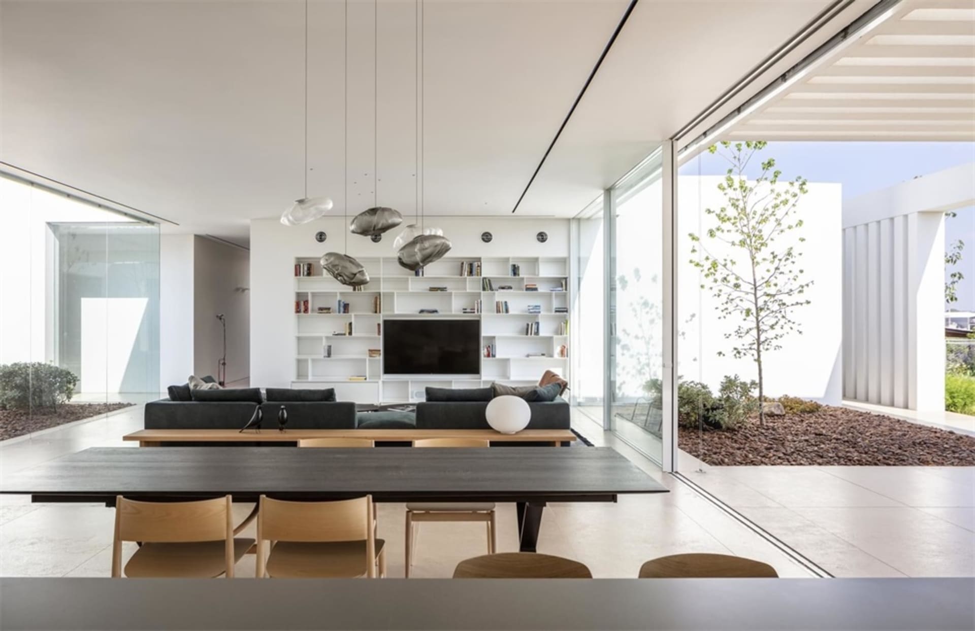 A modern living room featuring glass walls, a black table, and a white shelving unit with books and decor.