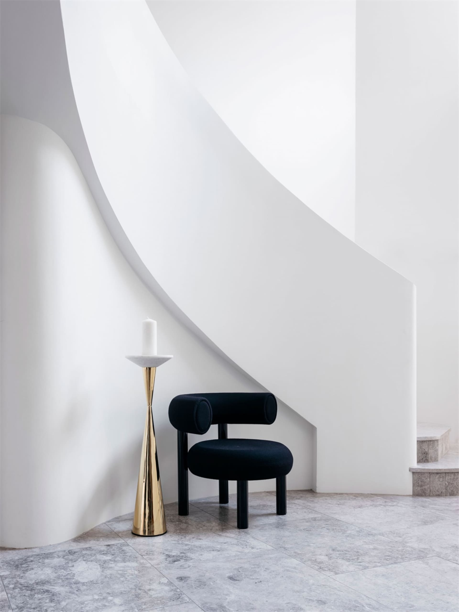 A minimalist staircase with a black upholstered chair on a marble floor.
