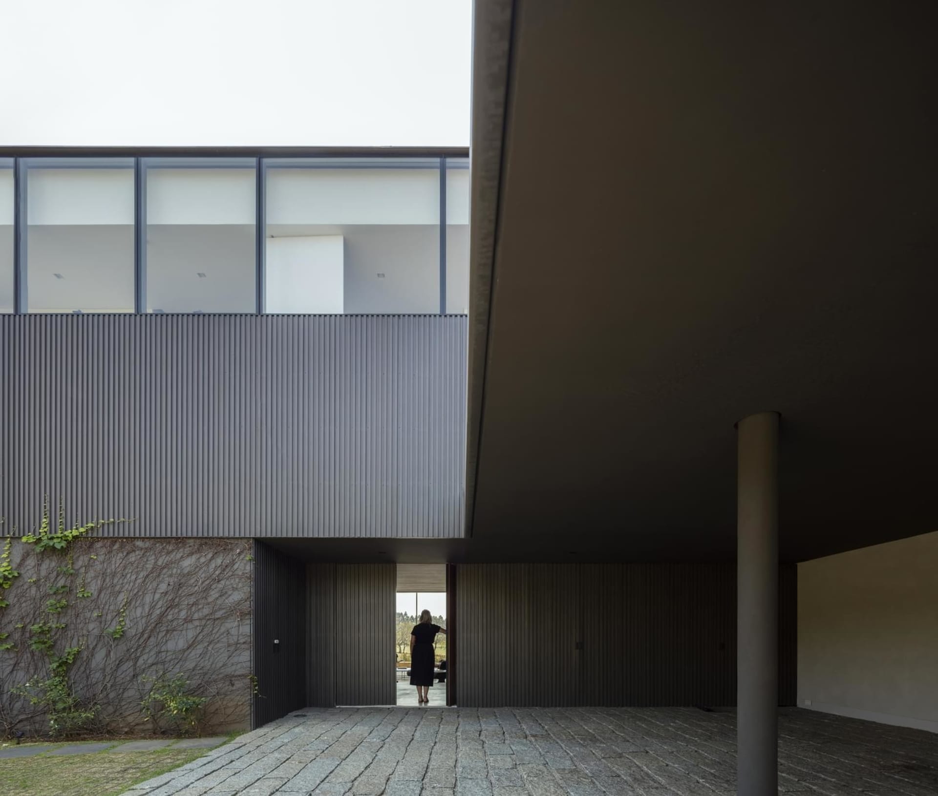 A modern residential exterior featuring metal-clad siding and a concrete floor.