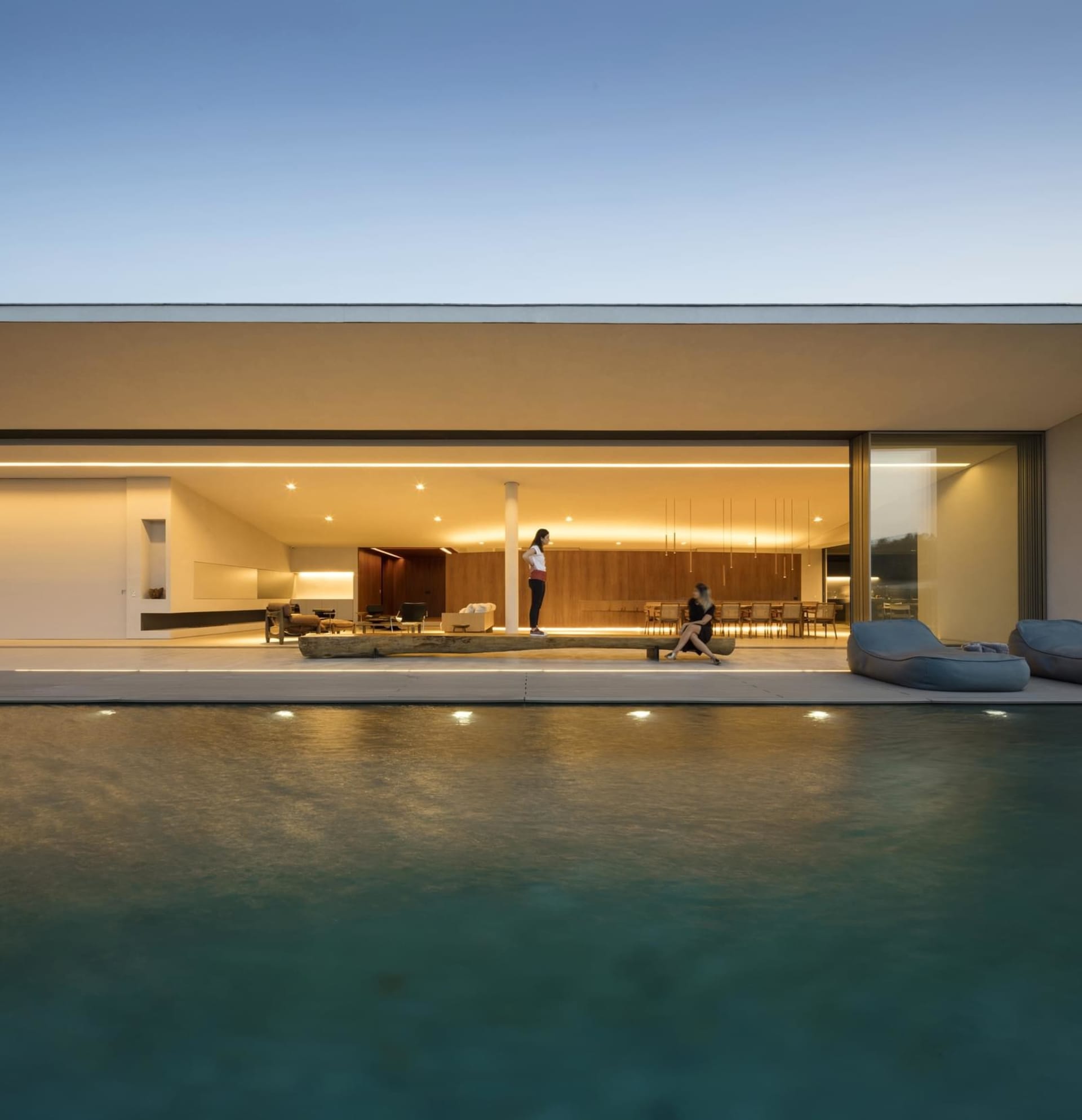 A modern residential poolside area with concrete walls and large glass doors.