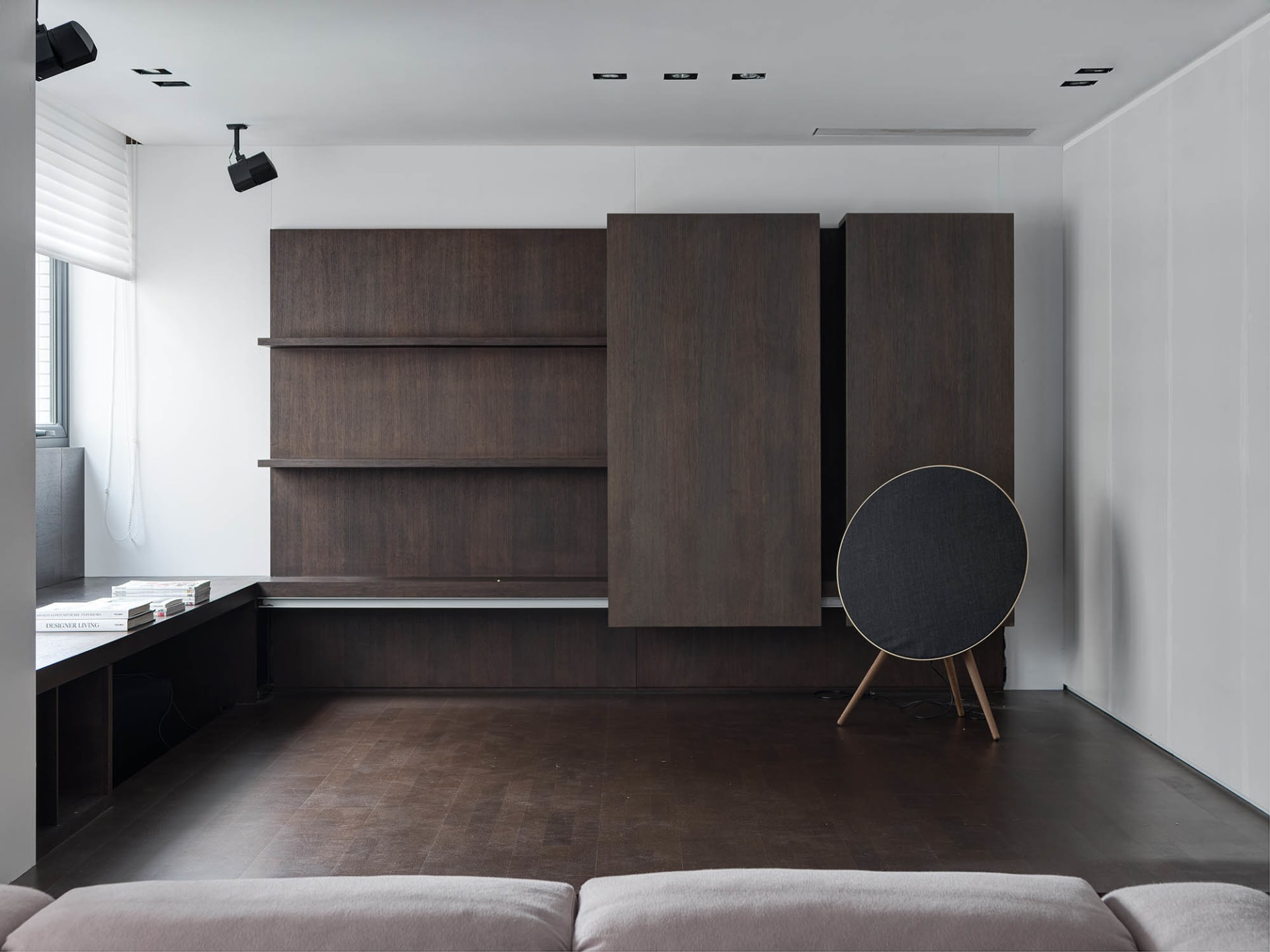 Modern minimalist living room with dark wood shelving, concrete floor, and leather sofa.