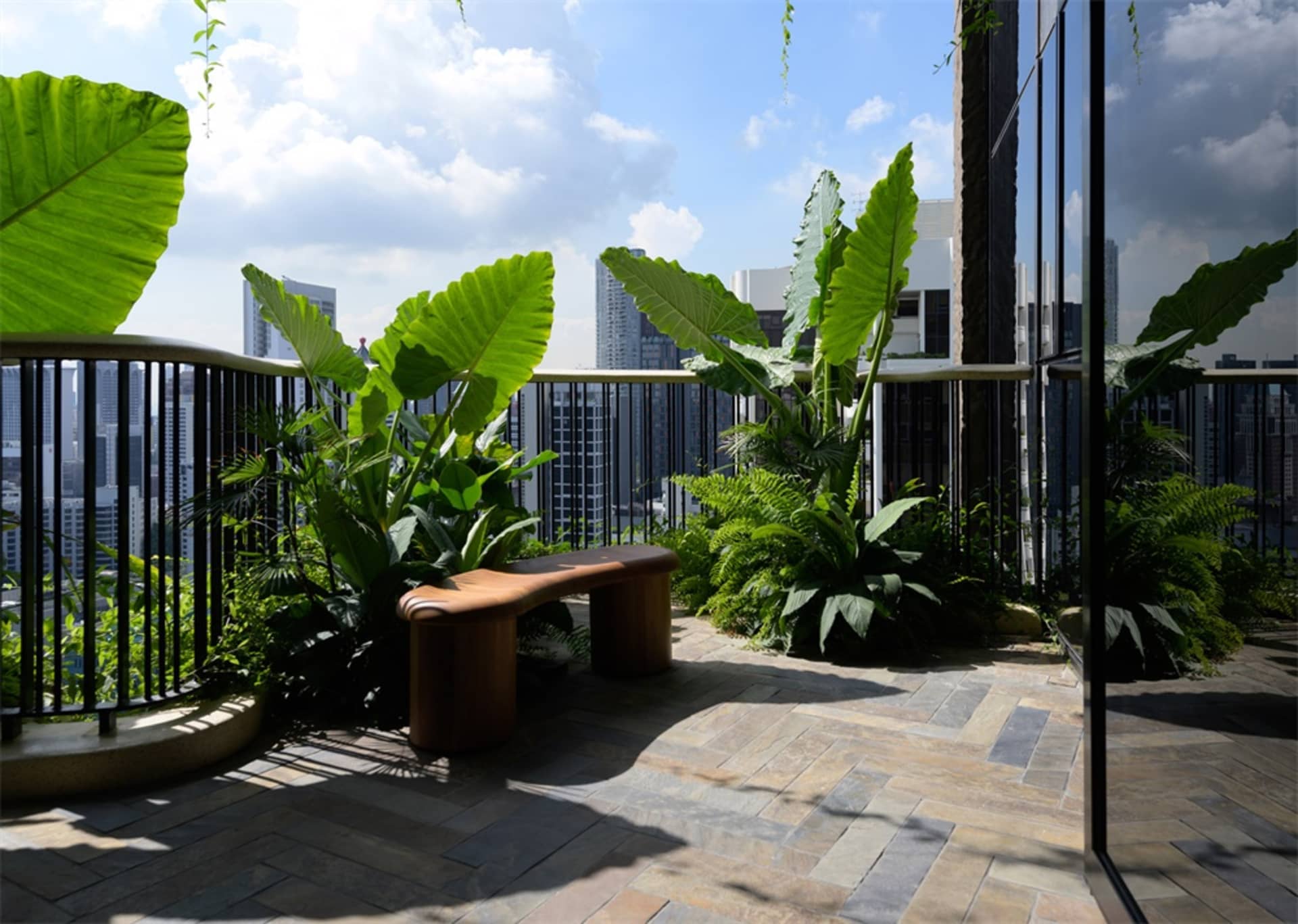 Modern rooftop garden with concrete structure and lush green plants on a sunny day.