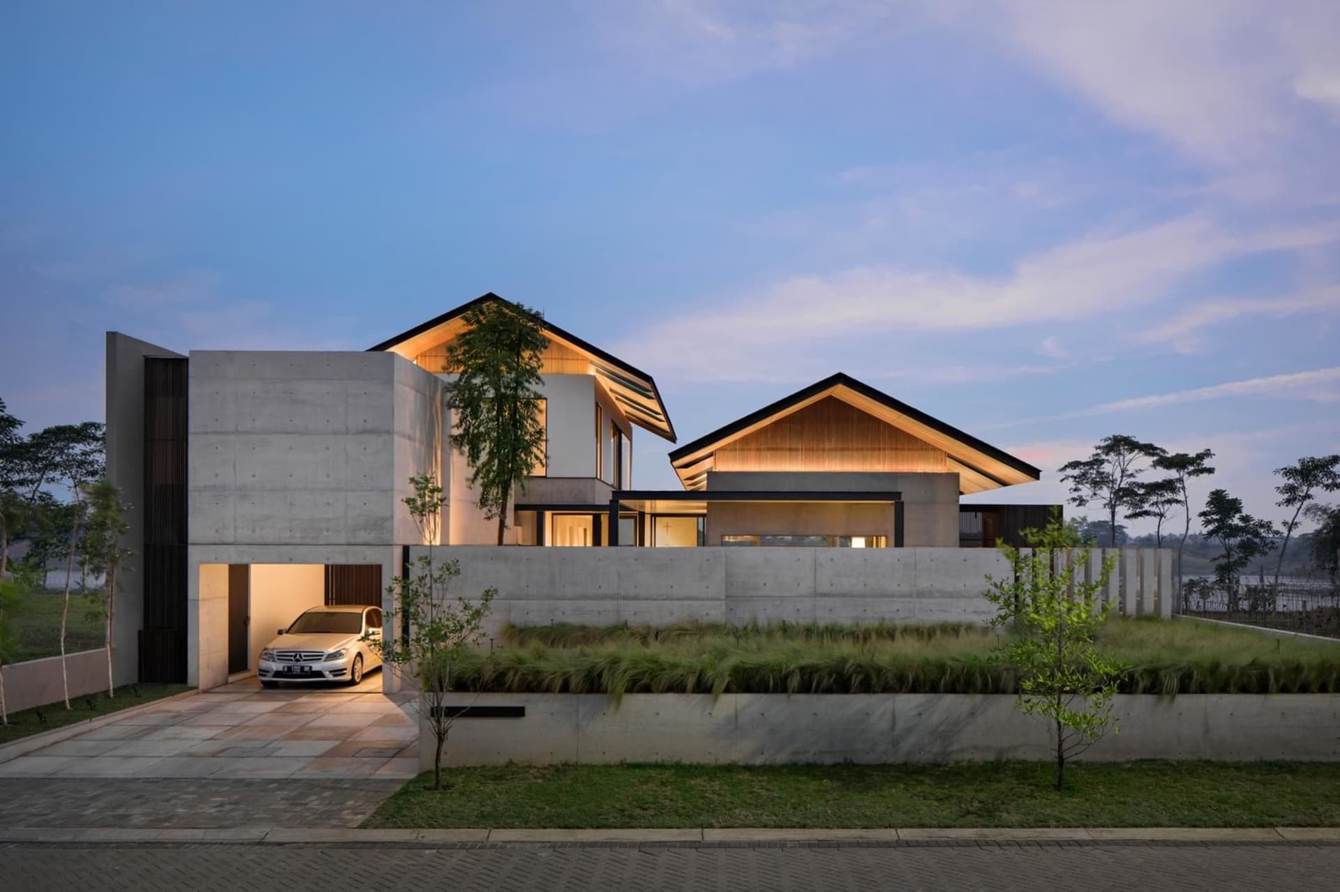 A modern residential home with a concrete exterior and minimalist design, illuminated by warm lights.