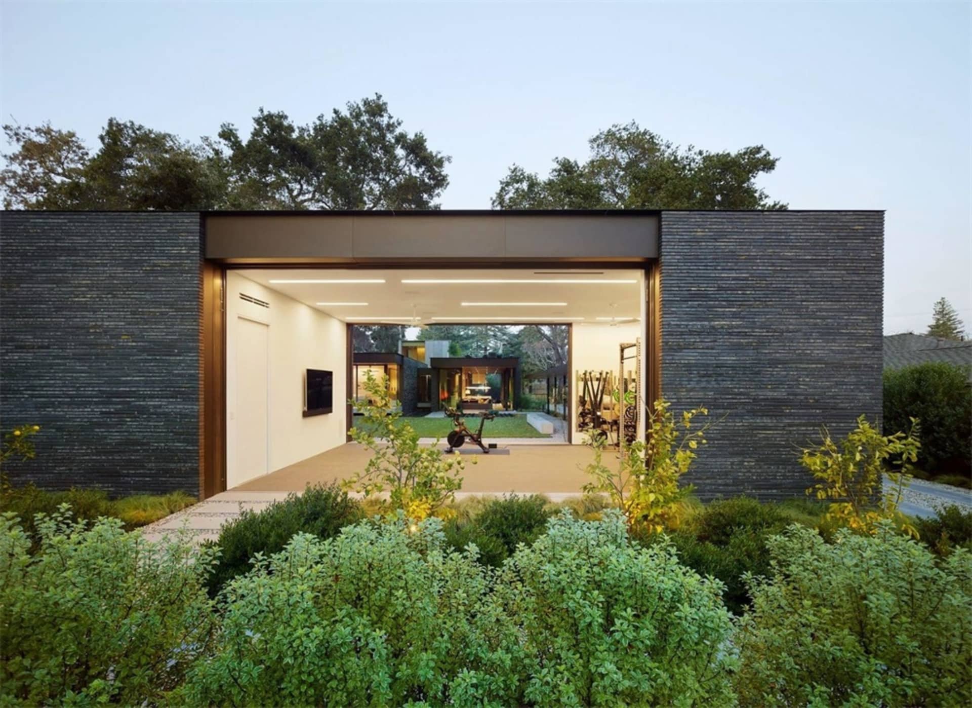 A modern minimalist residential garage with metal walls, glass doors, and stone ground.