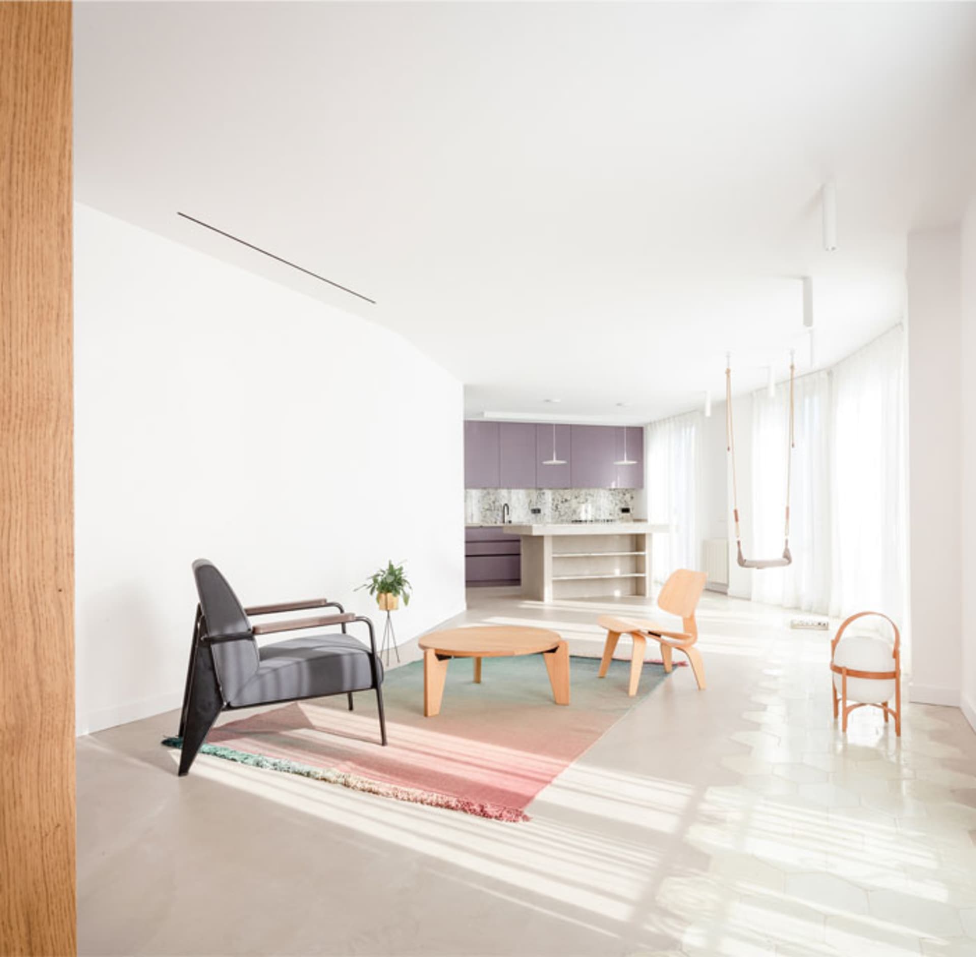 A minimalist living room featuring light-colored wood flooring and white walls, with a coffee table, armchairs, a small potte