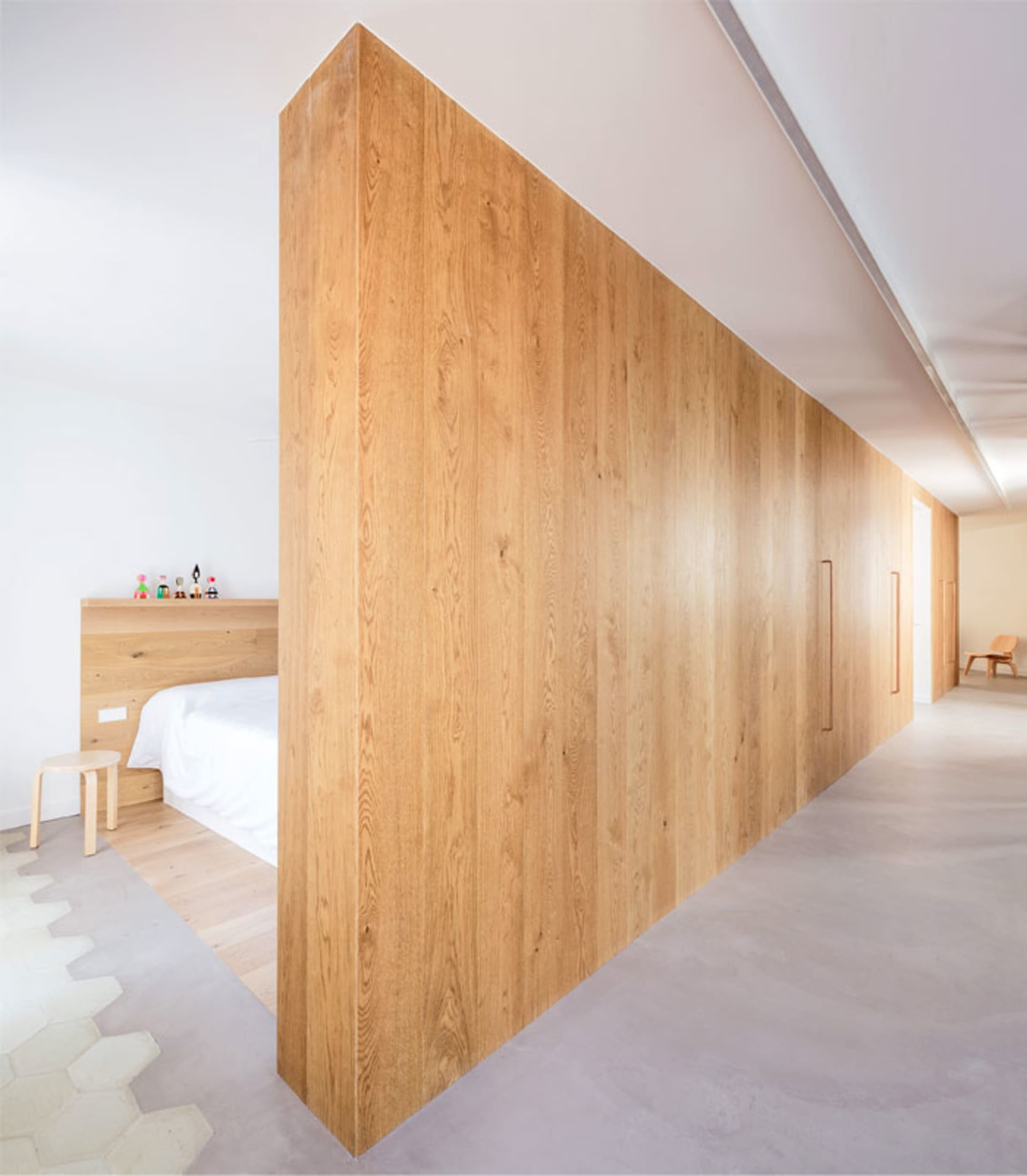 Spacious bedroom with white walls, natural wooden flooring, and a large wooden partition.