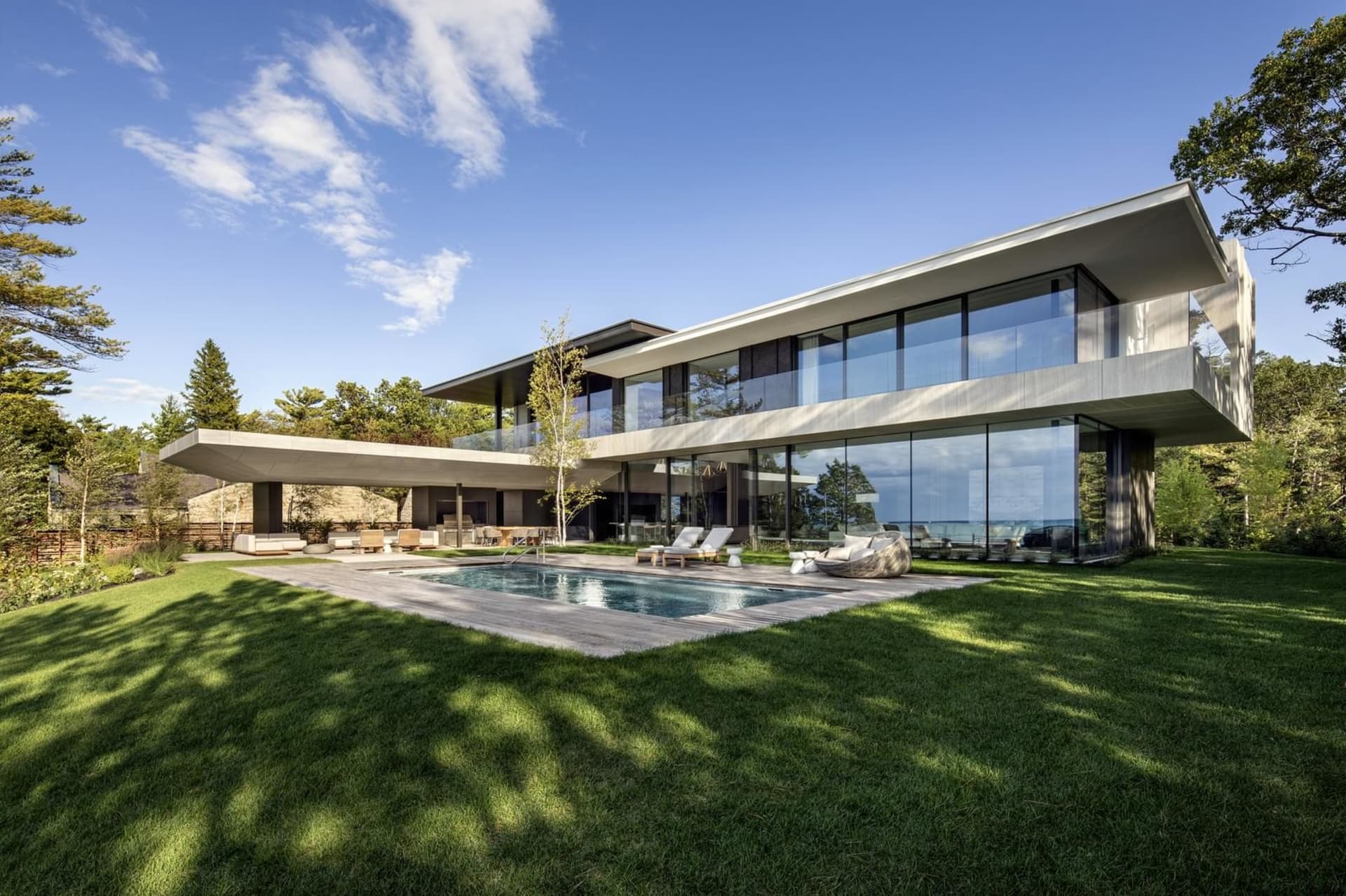 A modern minimalist house with a concrete exterior, glass walls, and a wooden deck.