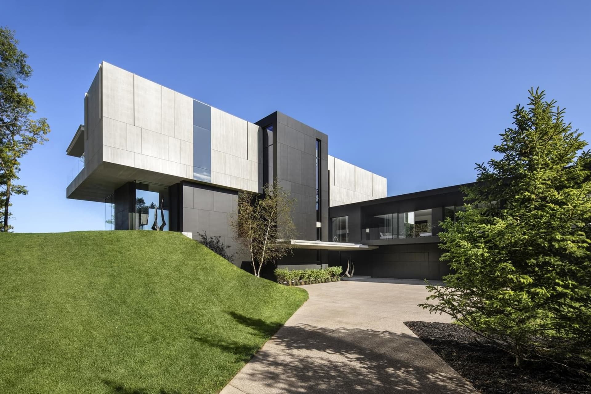 Modern, minimalist house with concrete and glass exterior, set on a grassy hillside.