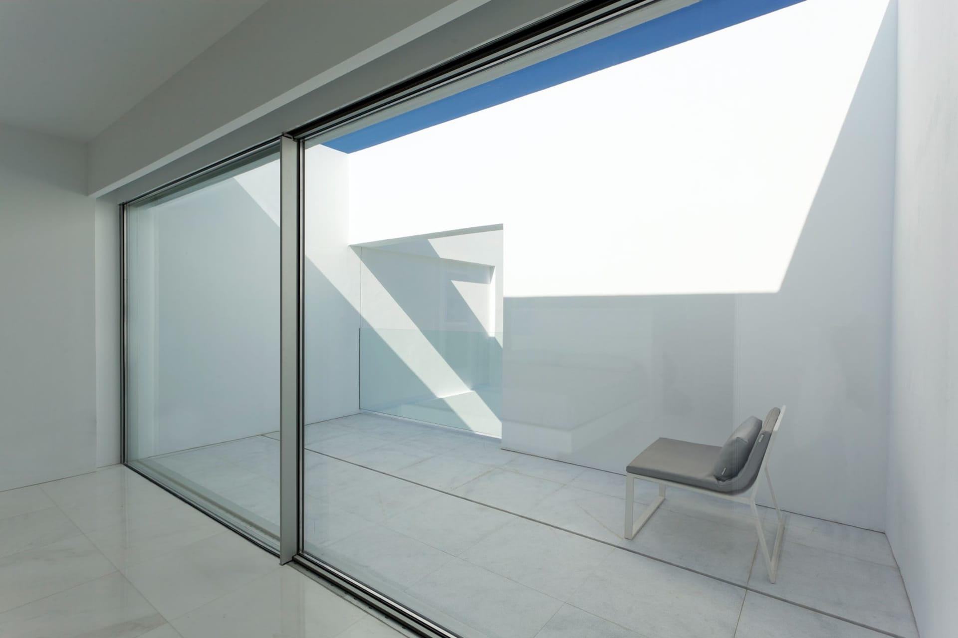 A minimalist balcony featuring glass walls, concrete floor, and metal accents.