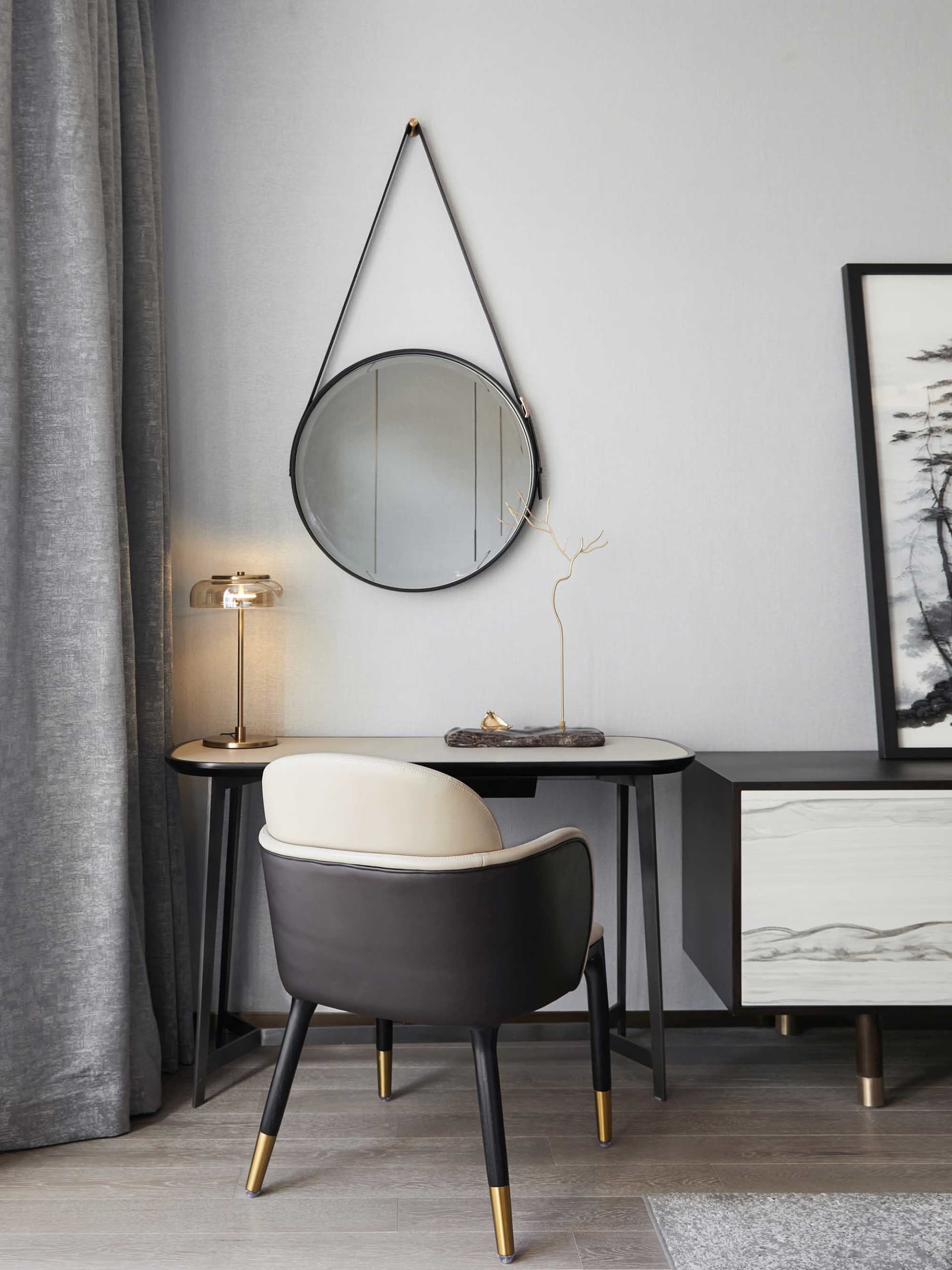 A modern minimalist home office desk with a round mirror, leather chair, and decorative lamp.