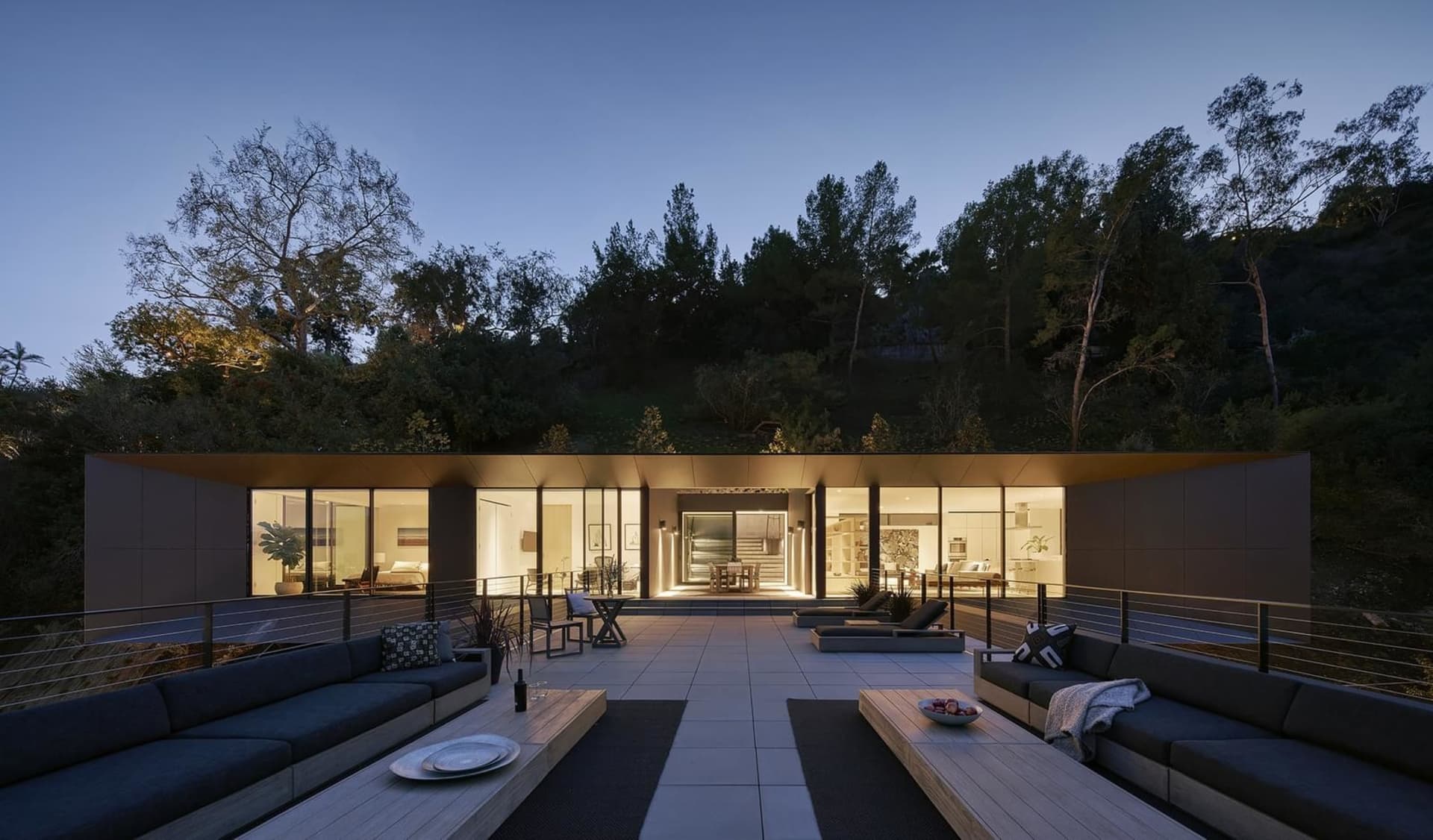 Modern outdoor patio furniture with metal frame and black cushions placed on a tiled patio surrounded by natural vegetation.