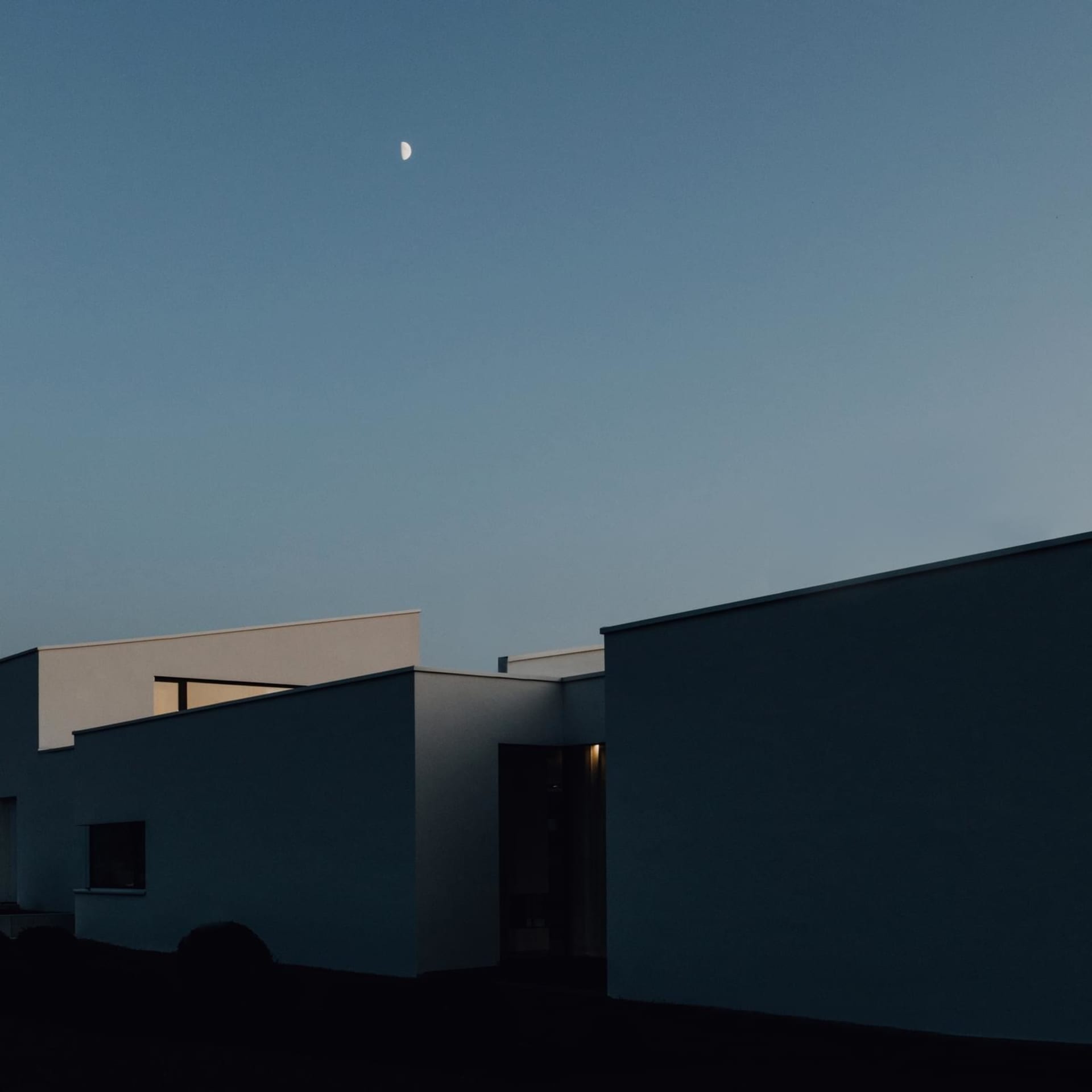 極簡風格的現代建築外觀，夜空懸掛一彎新月。