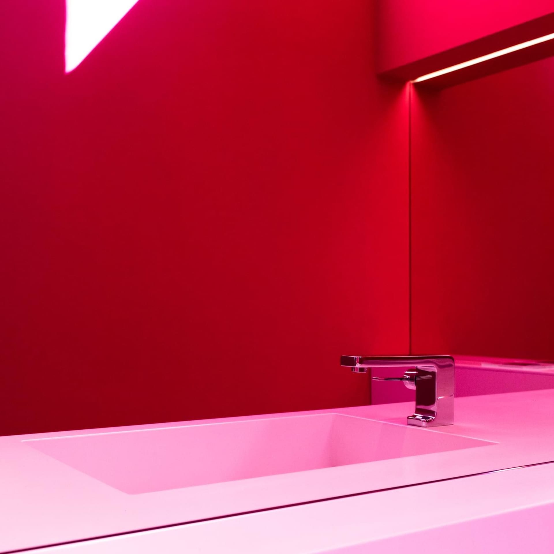 Modern minimalist bathroom with a white sink, faucet, and red lighting.