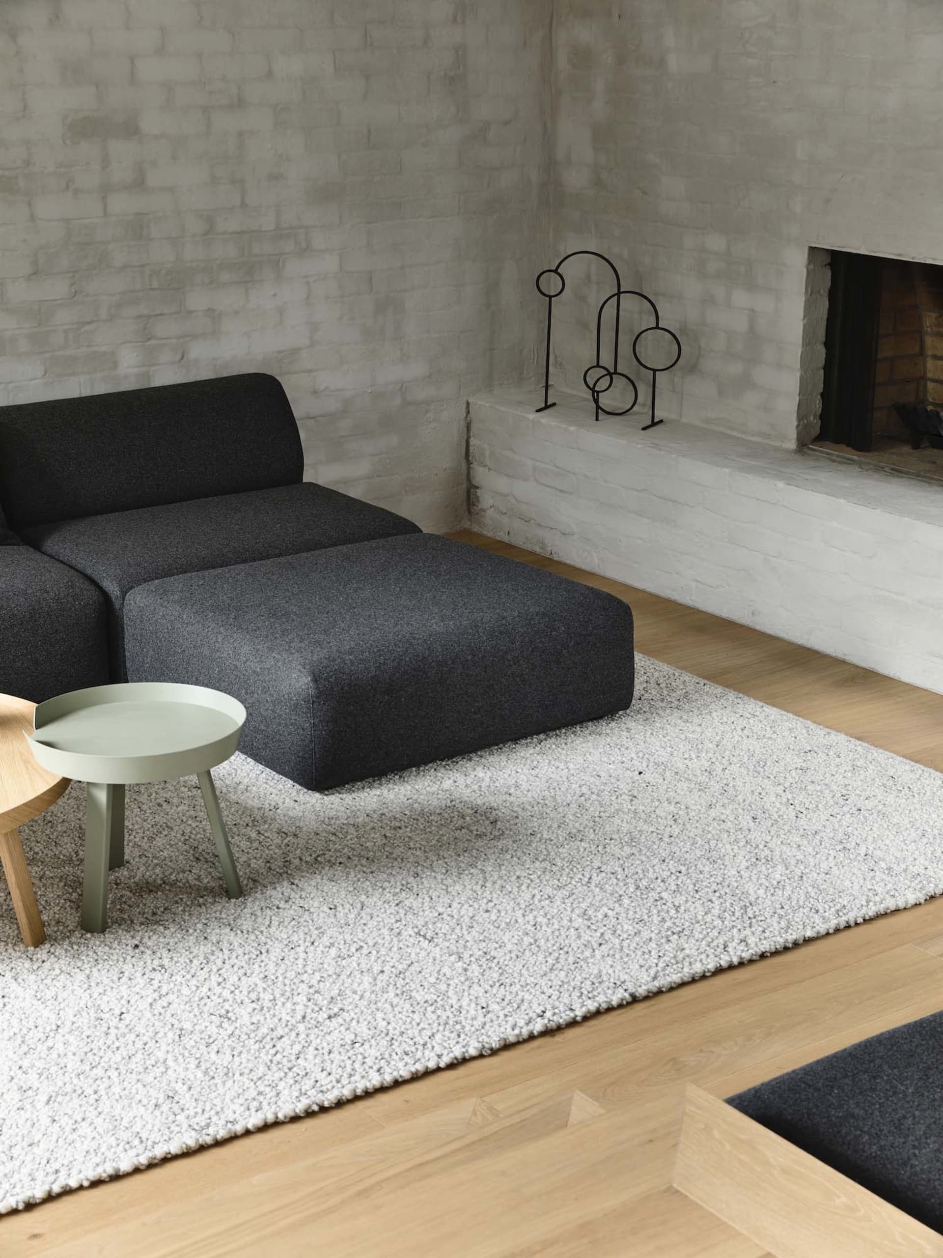 Modern minimalist living room featuring a wool rug, a dark grey modular sofa, a small round table, and a white fireplace with