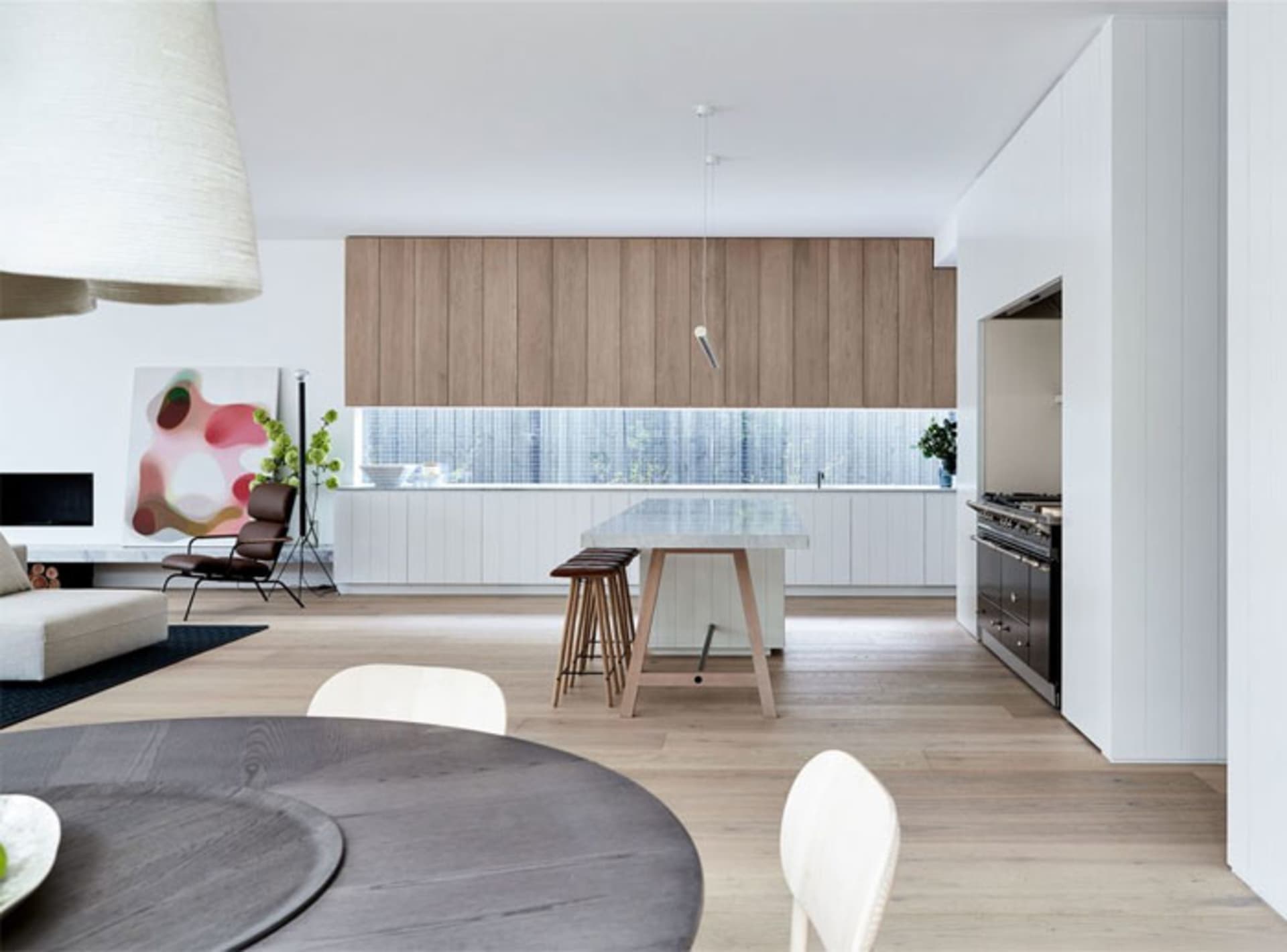 Modern residential space with white walls and wooden floors, featuring a kitchen area with wooden cabinets and white countert