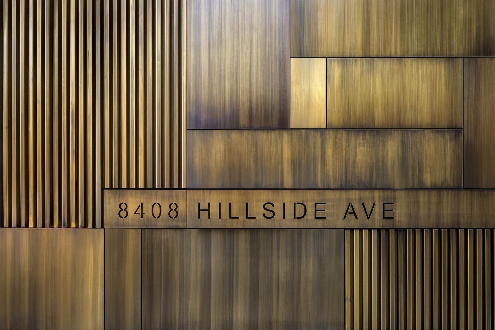 An architectural detail showing metallic brass signage with the address '8408 Hillside Ave'.