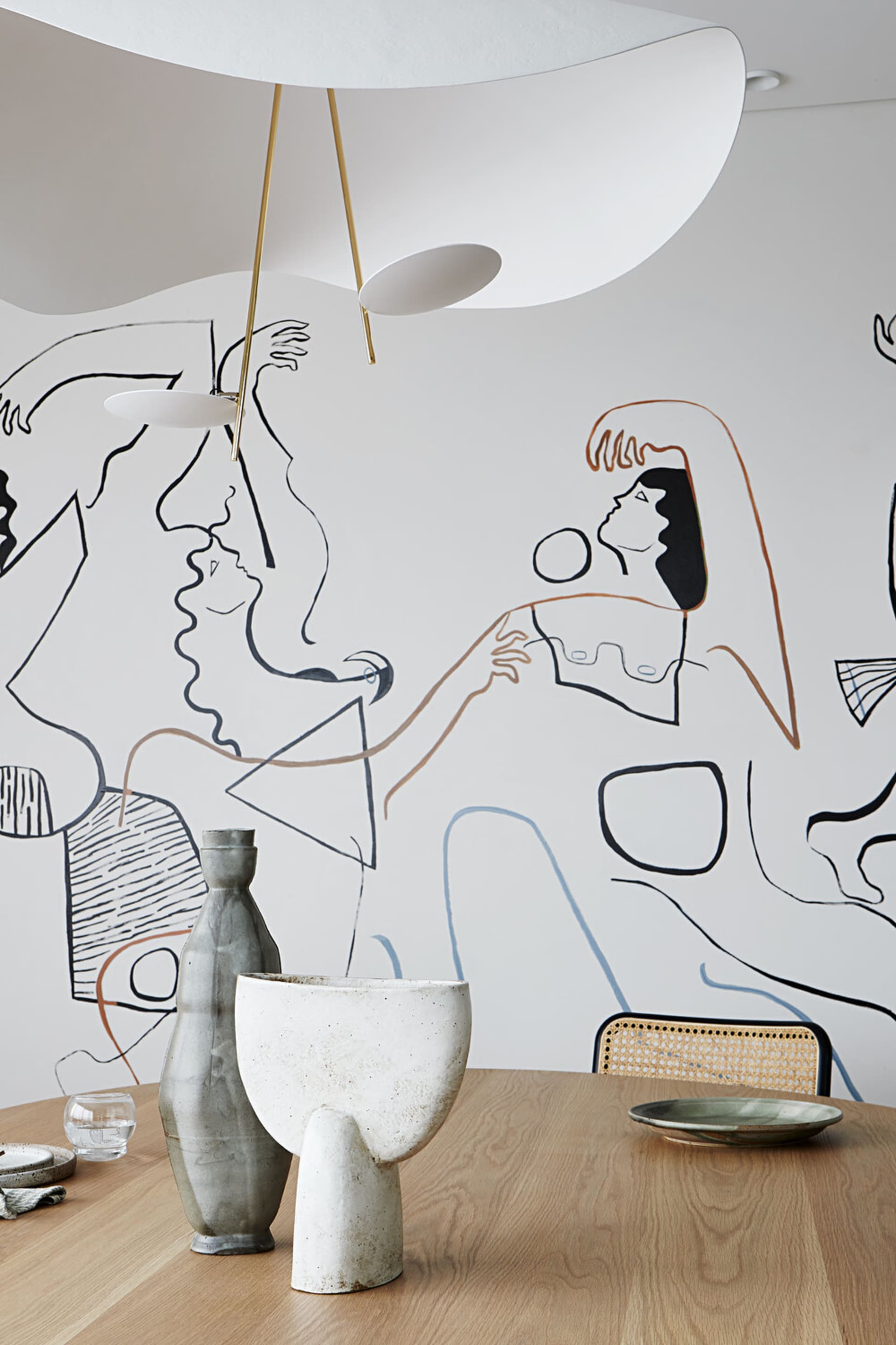 A modern dining room featuring ceramic tableware and a mural of abstract figures on the wall.
